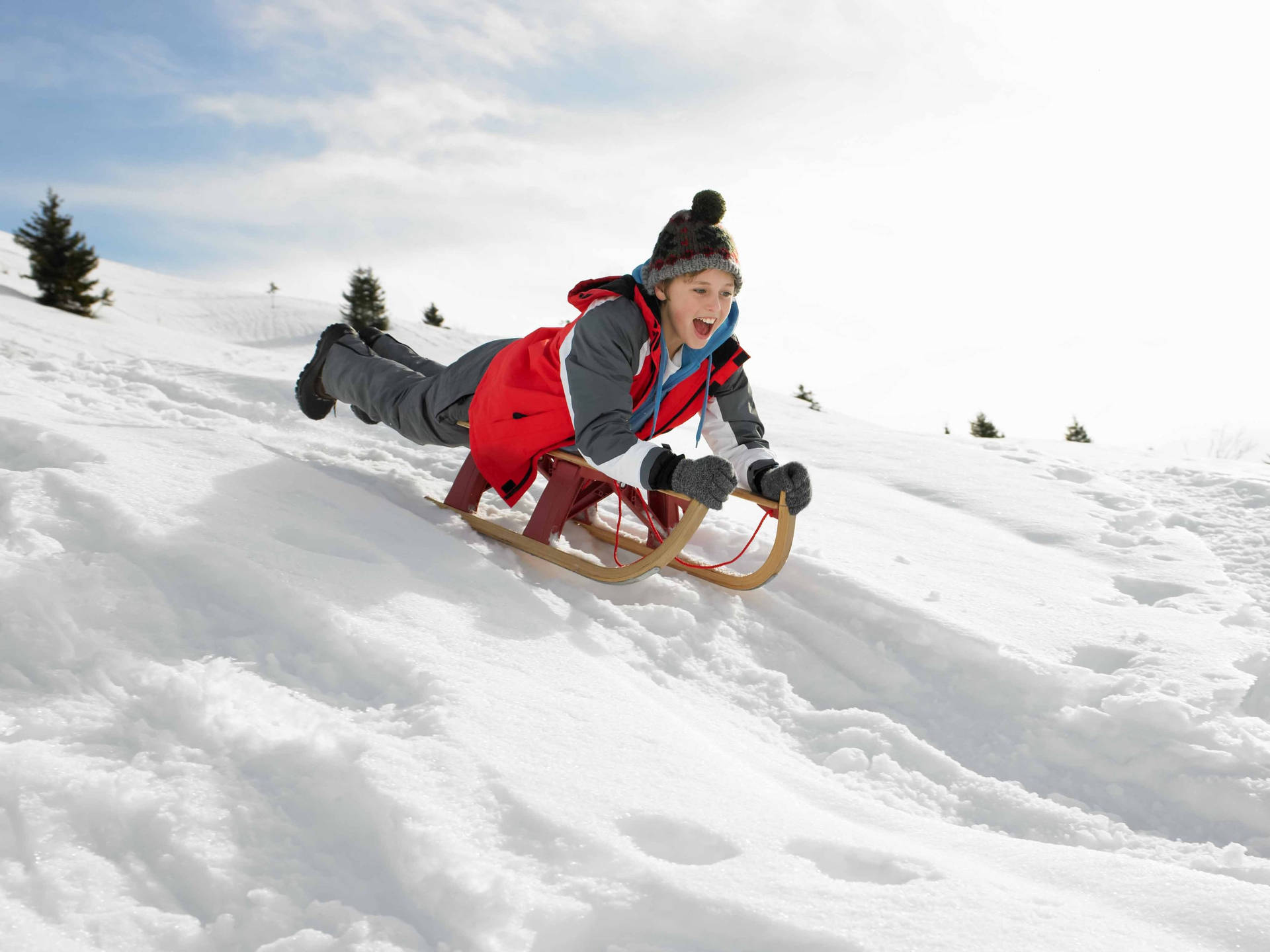 孩子穿著紅色外套和針織帽在雪坡上滑雪橇