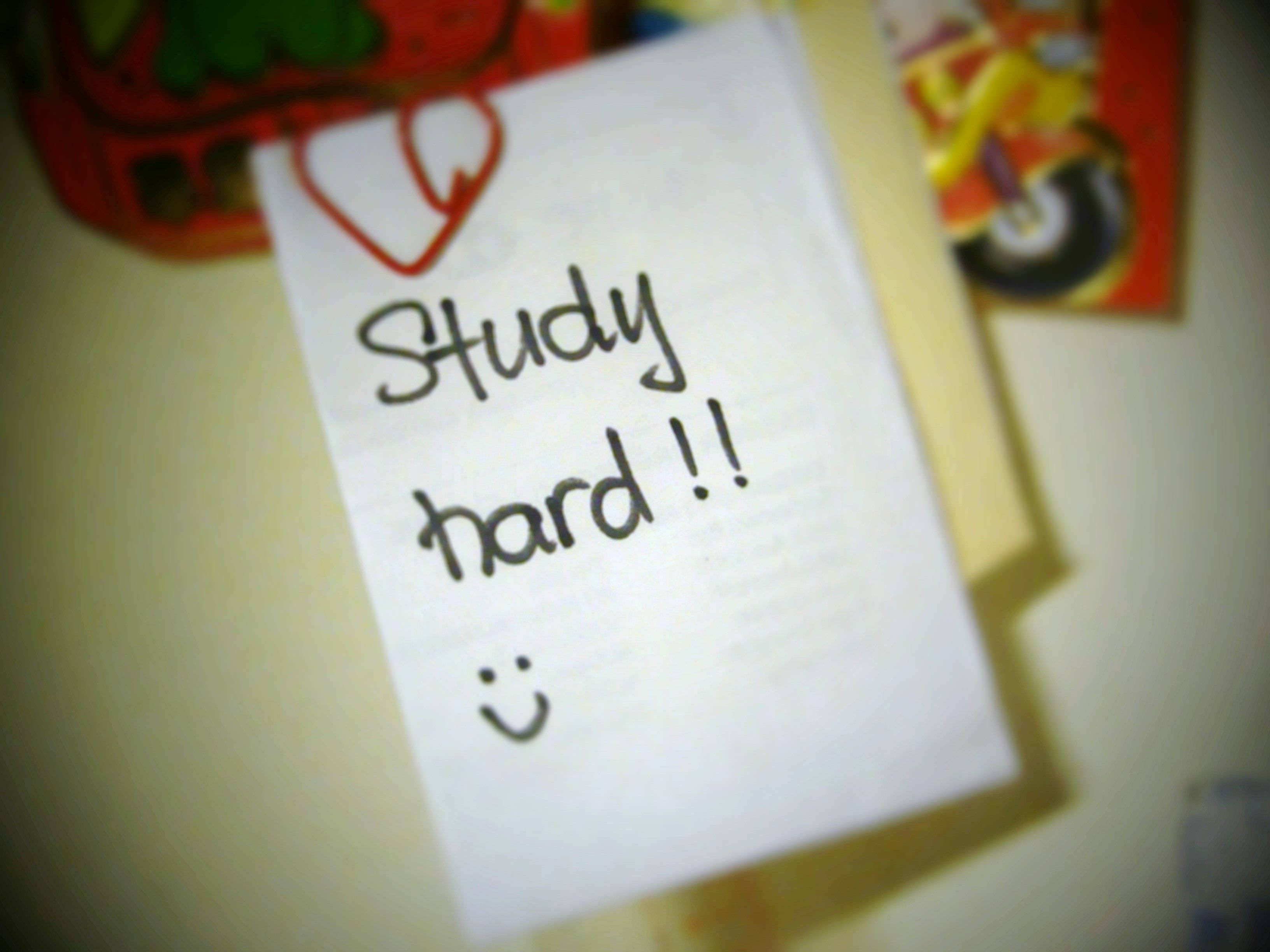 學習努力勵志語 壁紙 — 一張手寫便條，上面寫著「Study hard !!」和一個笑臉，用紅色心形夾子固定在牆上。