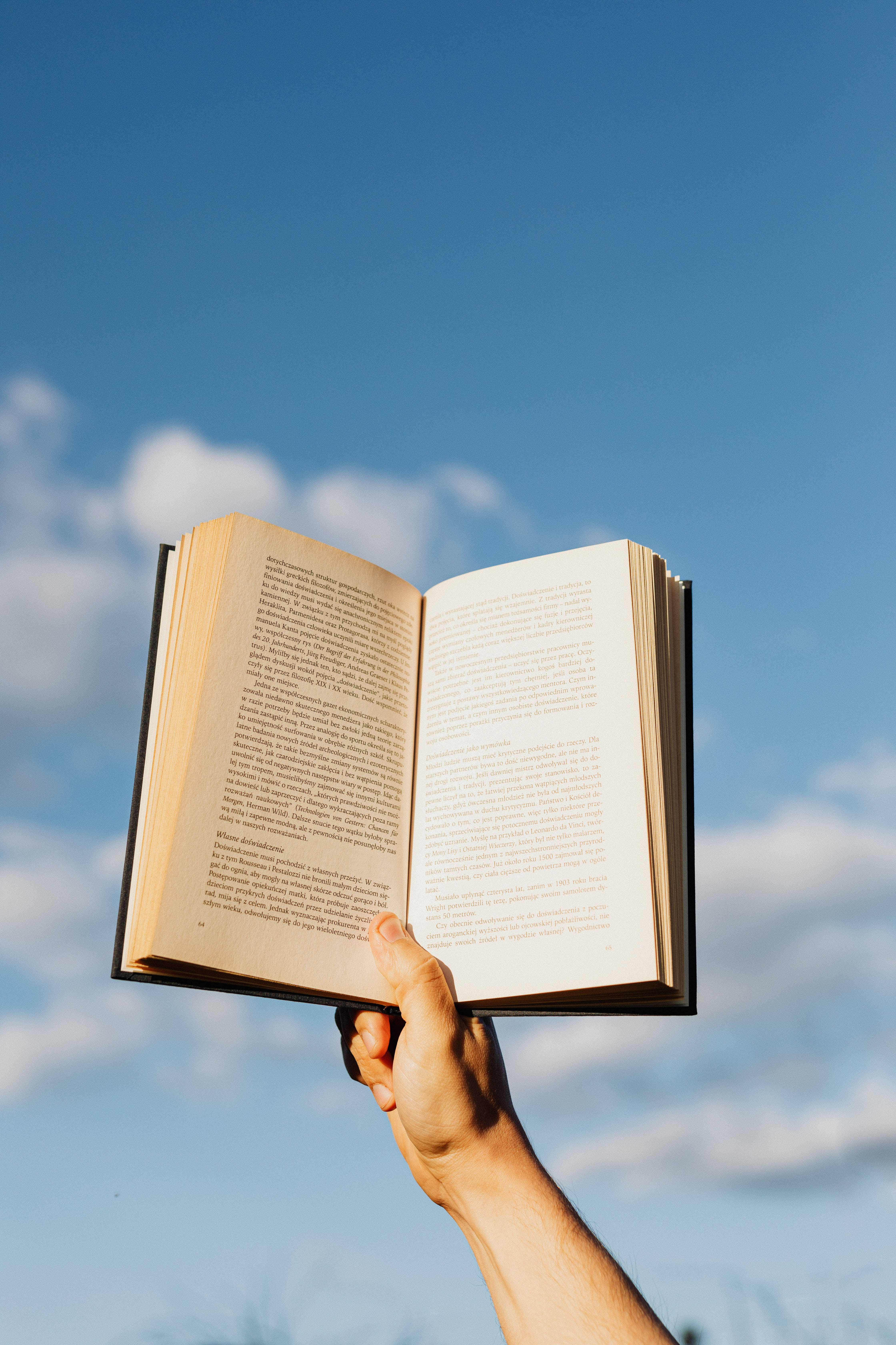 學習動力戶外 壁紙 — 一隻手拿著一本打開的書，背景是晴朗的藍天和白雲。