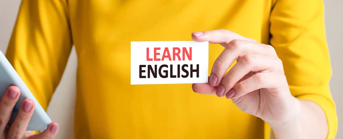學習英語的語言卡片攝影圖 壁紙 — 一個穿著黃色襯衫的人拿著一張寫著「學習英語」的卡片，同時拿著平板電腦。