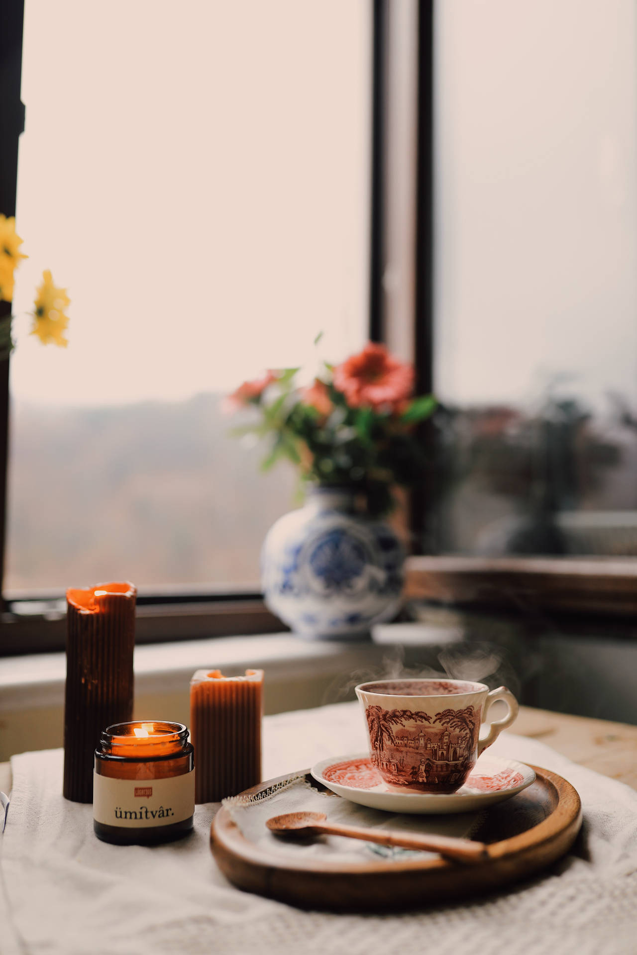 窗邊有茶、蠟燭和花朵的舒適室內場景。