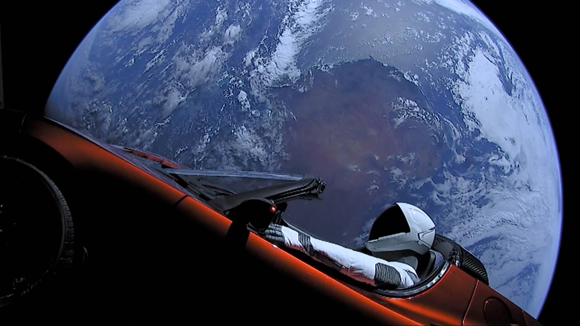 宇航員駕駛汽車於太空 壁紙 — 一名孤獨的太空人坐在流線型紅色太空船中，從太空的黑色虛空凝視著地球旋轉的藍白雲層。