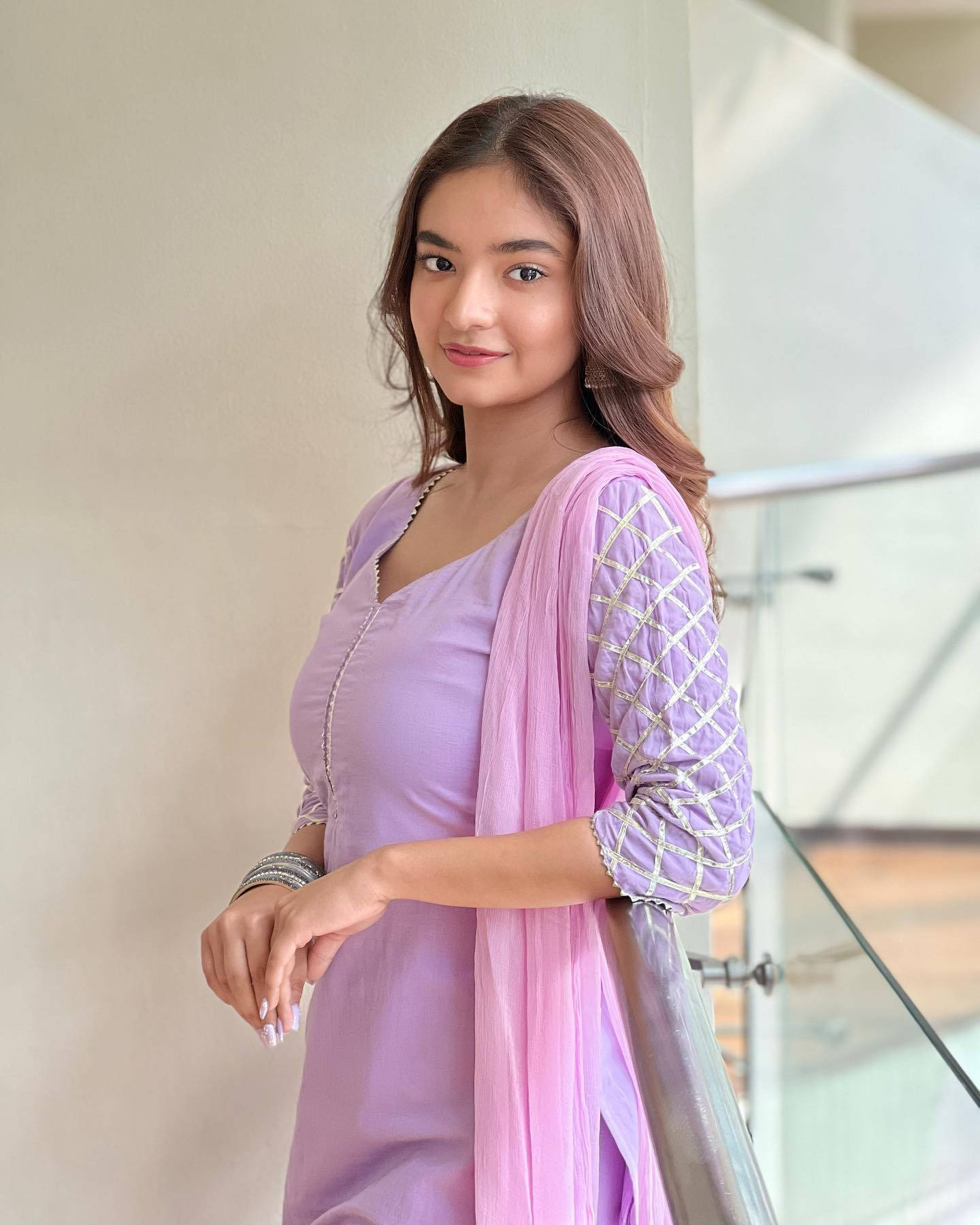 身穿薰衣草色傳統服飾的年輕女性在室內玻璃欄杆旁微笑。