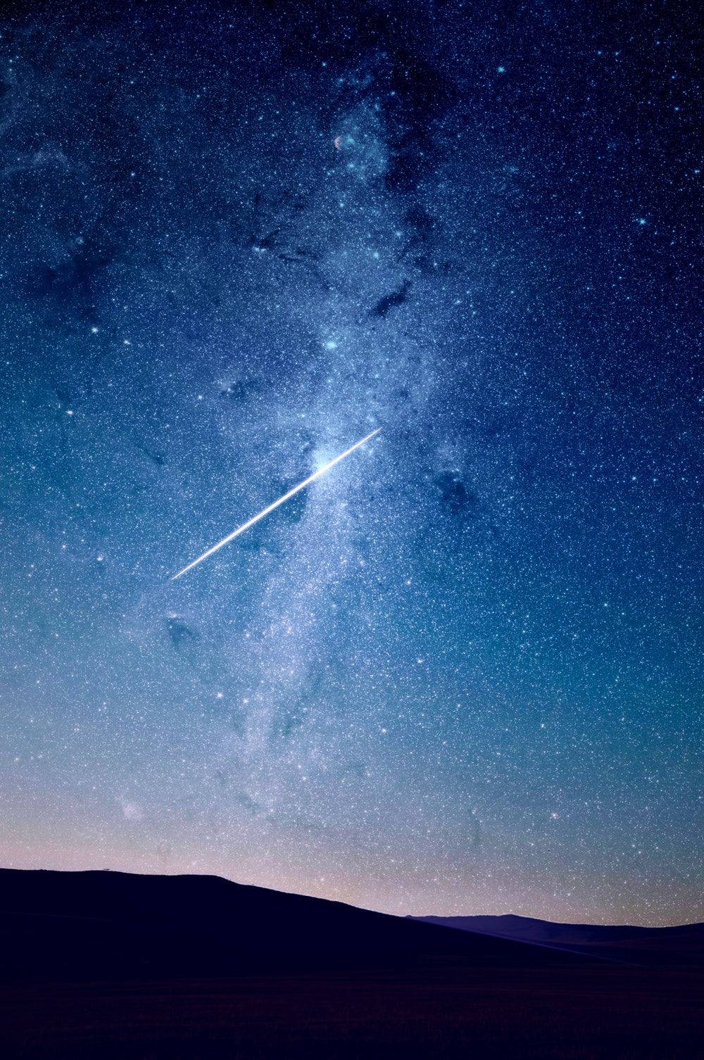一顆明亮的流星在黑暗山丘上方的星空中留下一道軌跡。