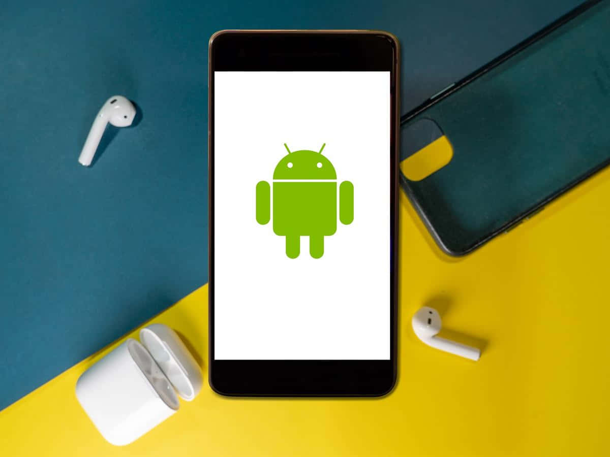安卓的鮮豔色彩與大膽圖案 壁紙 — 一部顯示綠色Android機械人標誌的智能手機放在鮮黃色和藍綠色的表面上，附近有白色無線耳機。