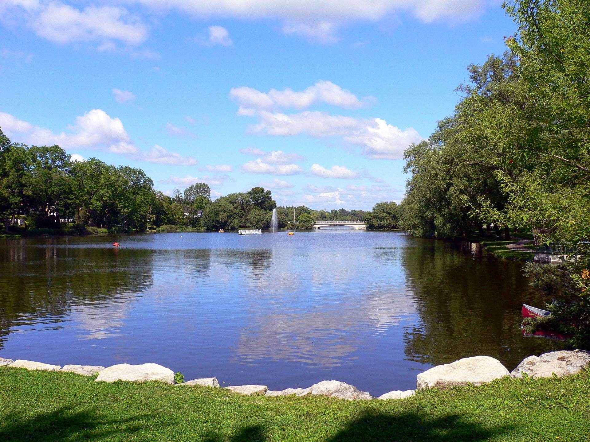 安大略公園風景 壁紙 — 一個寧靜的湖泊，四周環繞著茂密的綠色樹木，上方是明亮的藍天和蓬鬆的白雲。