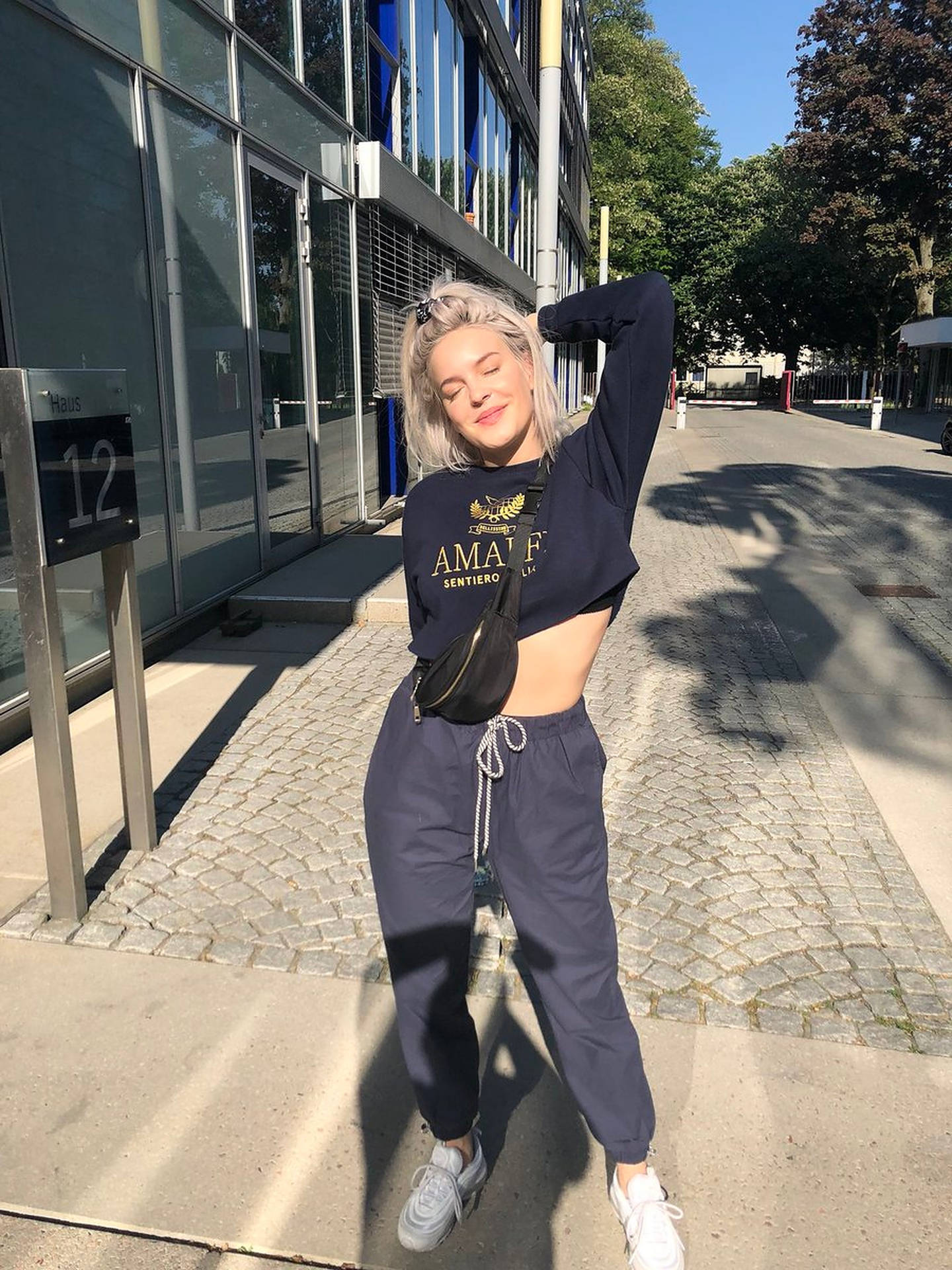 年輕女性穿著休閒街頭服飾，在現代建築附近的陽光人行道上擺姿勢。