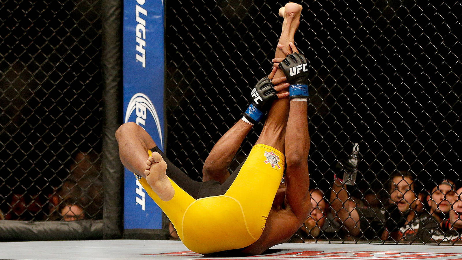身穿黃色短褲的MMA拳手在UFC八角籠內施展腿鎖。