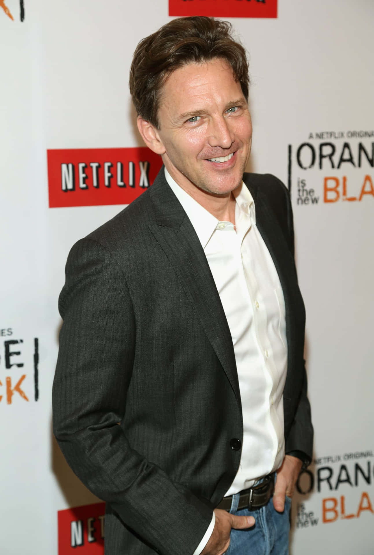 演員在Netflix活動中對著鏡頭微笑，背景為Orange is the New Black。