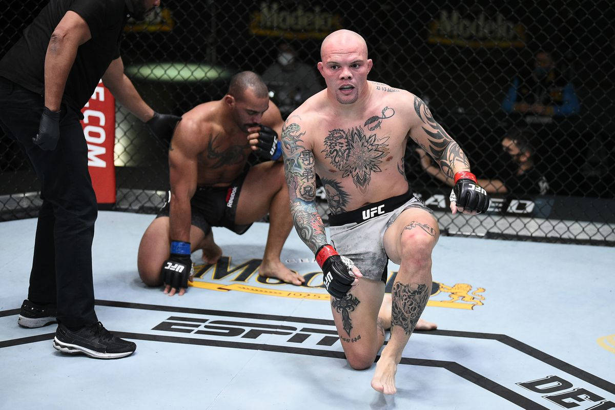 安東尼·史密斯站起 壁紙 — 一位紋身MMA拳手在八角籠中跪地勝利，對手在墊上投降。