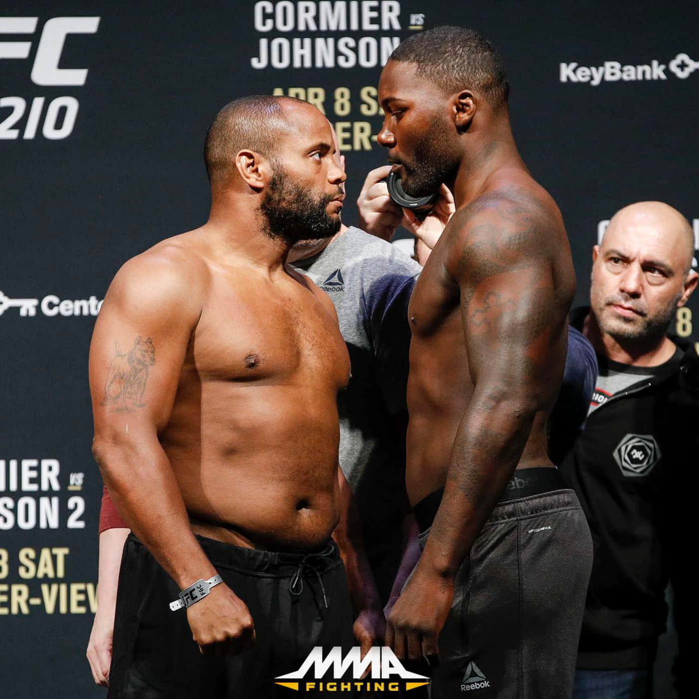安東尼·約翰遜與丹尼爾·科爾米爾 UFC 210 壁紙 — 兩名肌肉發達的MMA拳手在明亮的攝影棚燈光下於稱重活動中激烈對峙。