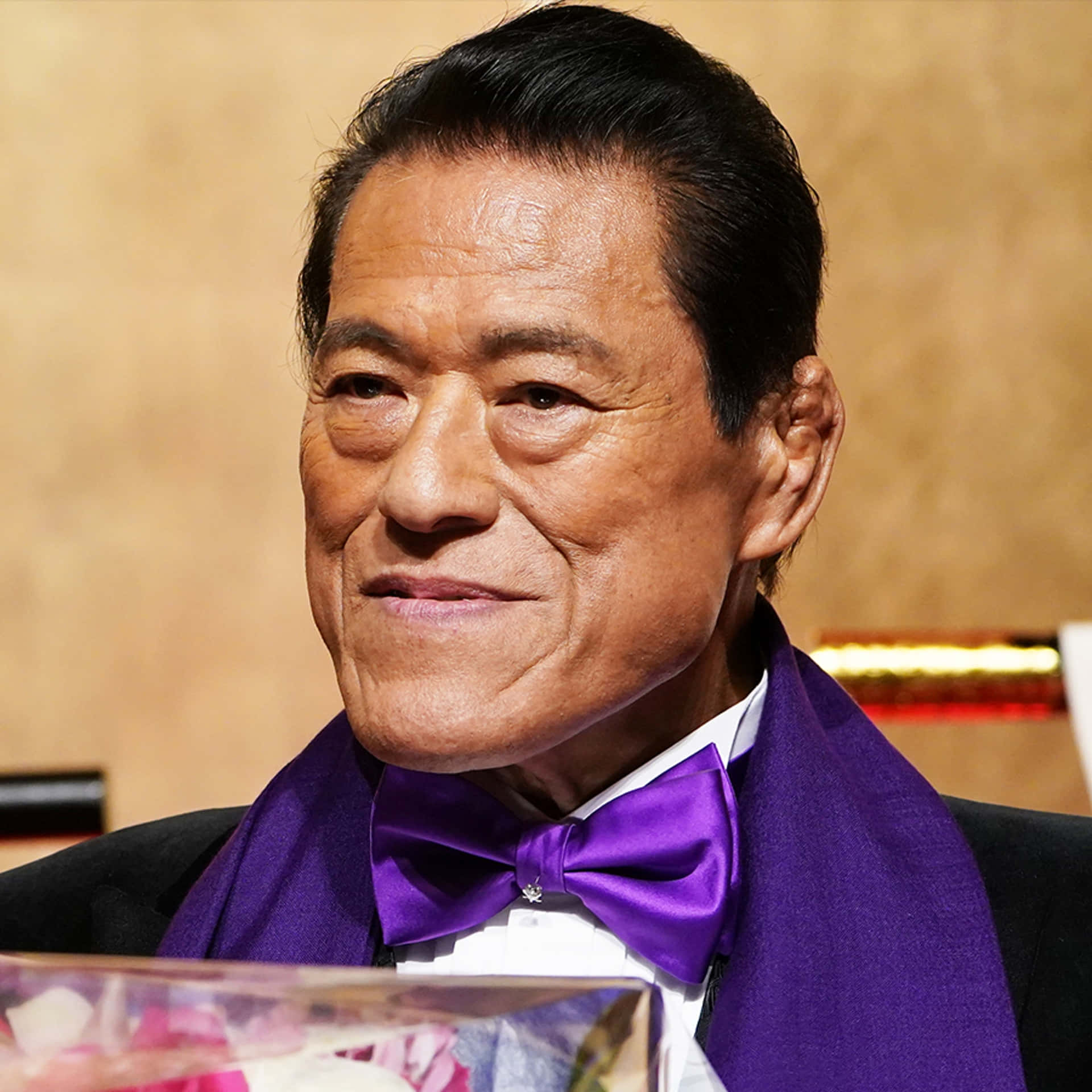 一位優雅的老年男士身穿燕尾服，搭配紫色領結和圍巾，在活動中微笑。