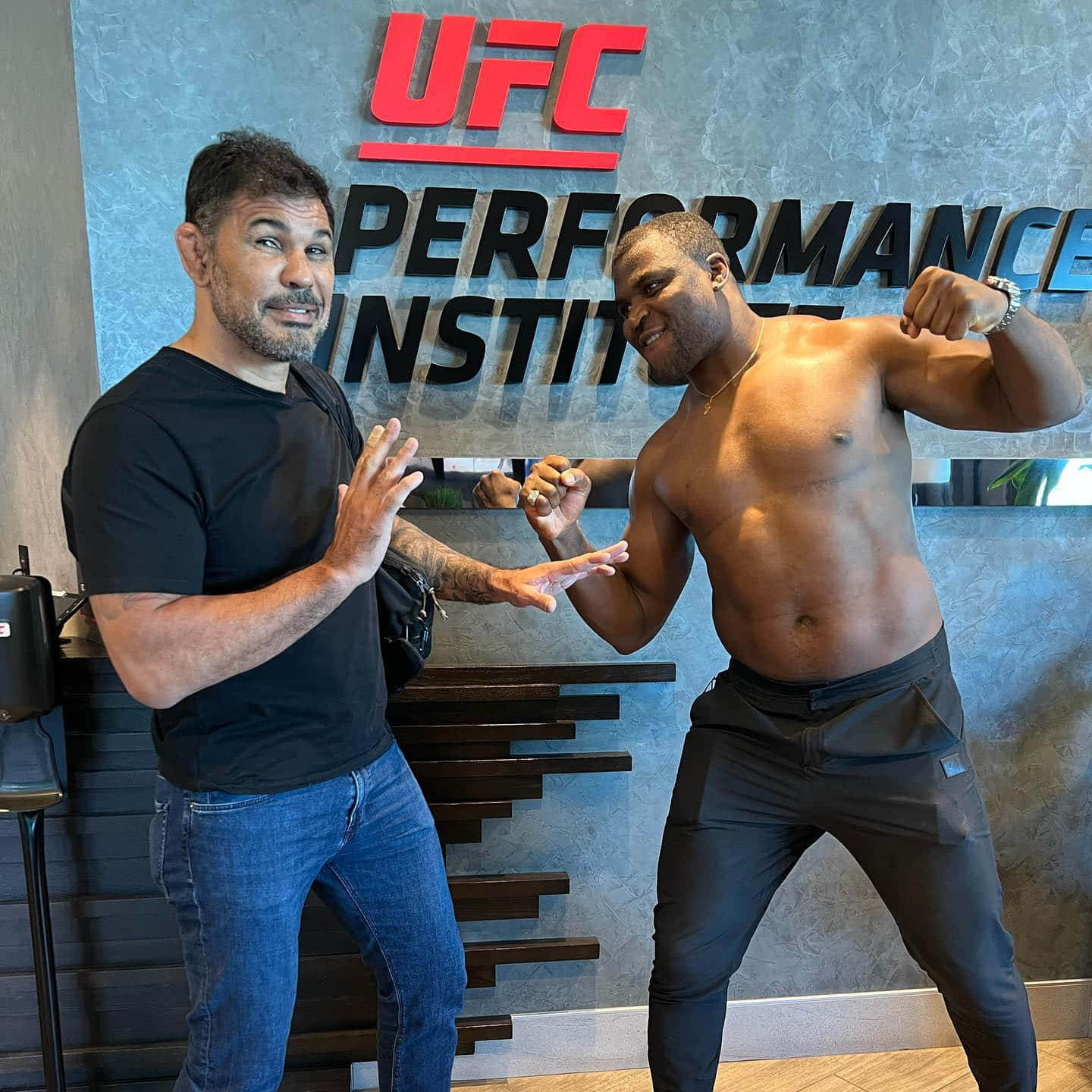 兩個男人在UFC Performance Institute擺姿勢，一個赤裸上身展示肌肉，另一個做手勢。