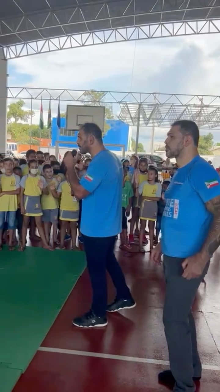 兩名男子在遮蓋運動場中與孩子們交談。