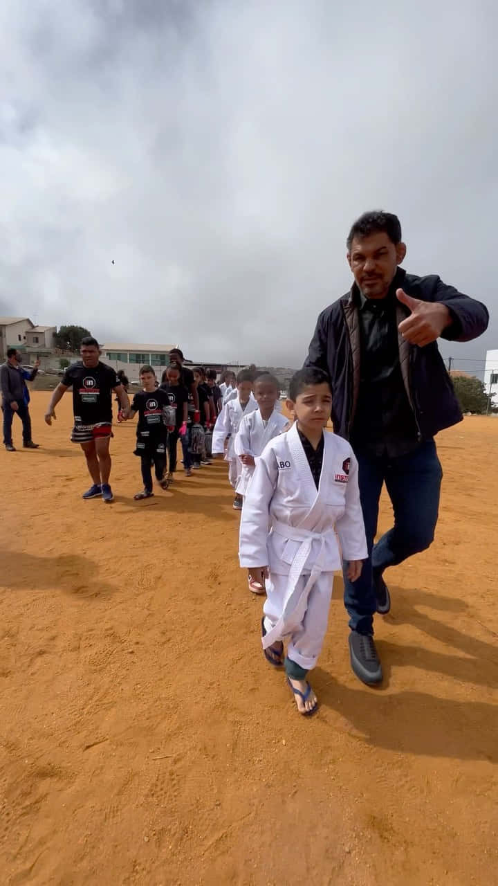 一名武術教練和小孩在塵土飛揚的場地上一起行走。
