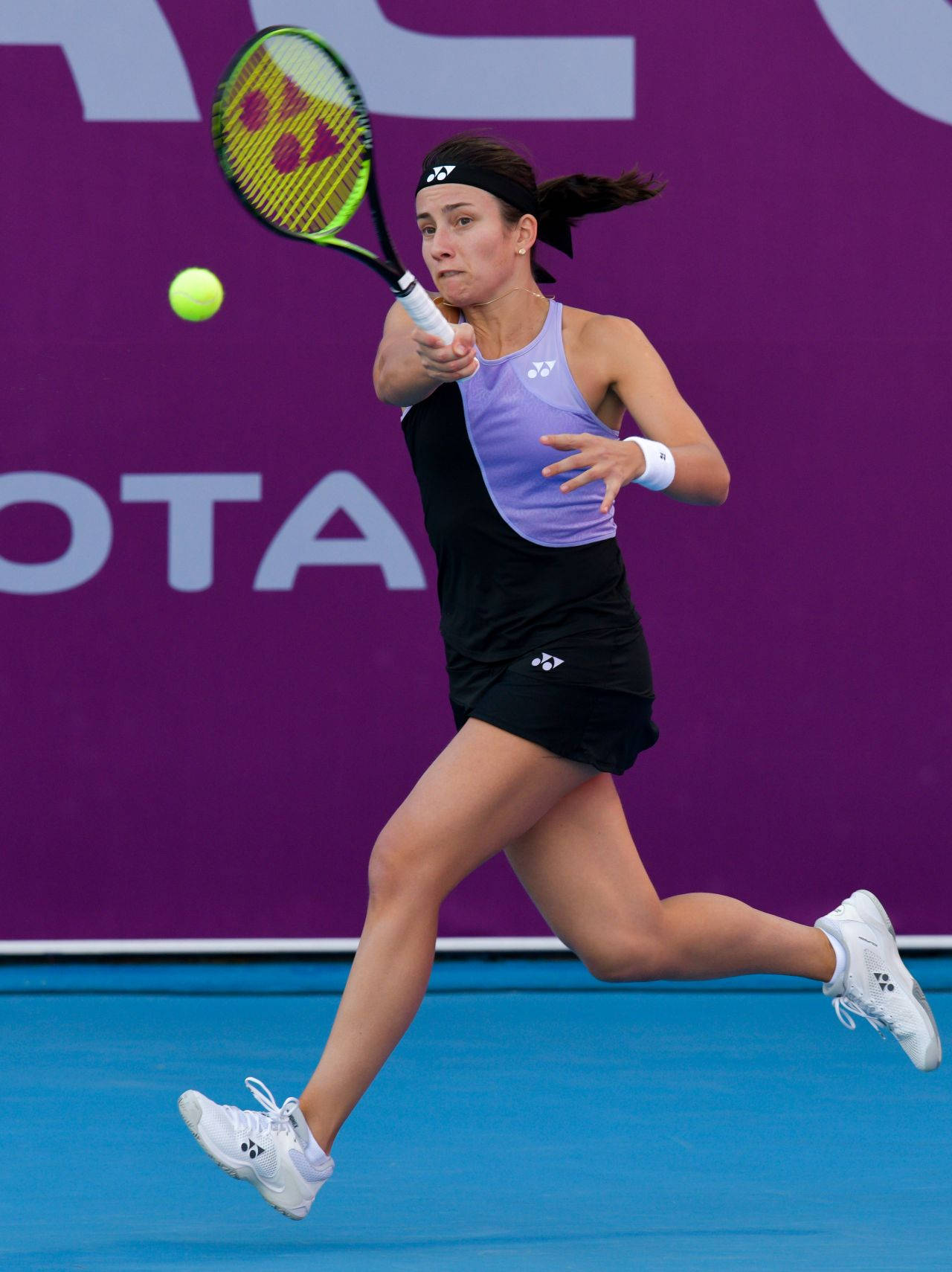 安納斯塔西婭·塞瓦斯托娃衝向球 壁紙 — 一位女性網球選手在運動中揮拍擊向一個亮黃色的球，球場是鮮明的藍色，背景是紫色牆壁。