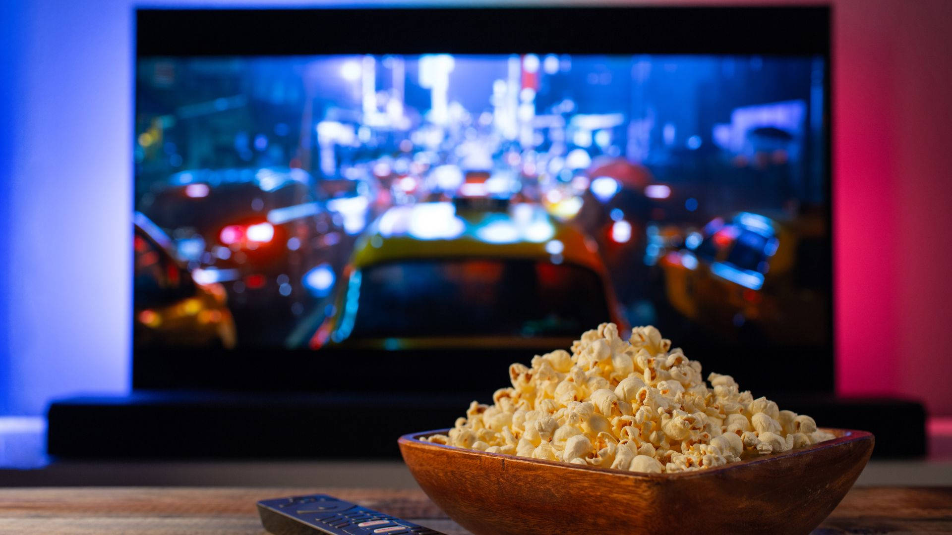 安裝電視觀看Popcorn Time 壁紙 — 一個木碗裝著的爆谷放在電視機前，電視顯示模糊的夜間城市街道，車燈閃爍。
