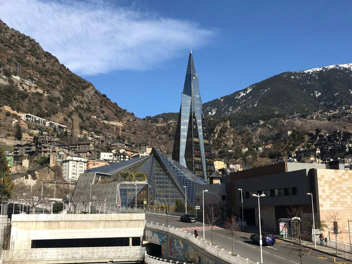 山城中的現代玻璃建築，背景有白雪覆蓋的山峰和下方的道路。