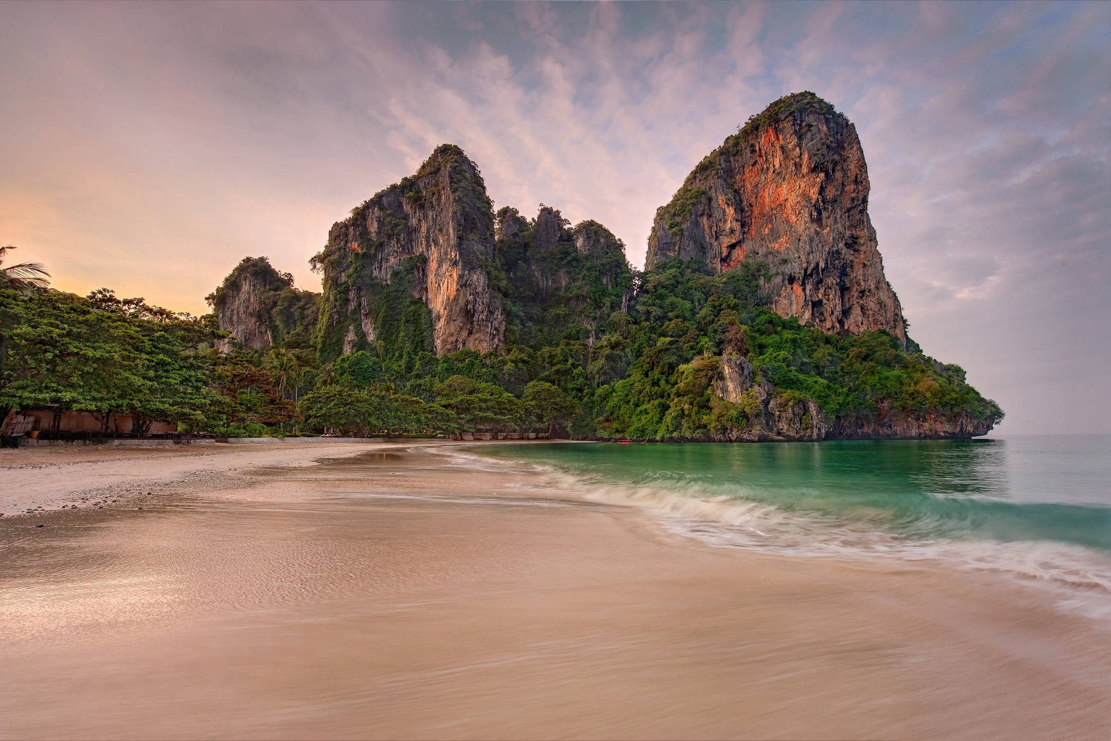 安達曼海 壁紙 — 日落時分寧靜的熱帶海灘，碧綠的海浪拍打著金色沙灘，背景是叢林覆蓋的高聳石灰岩懸崖。