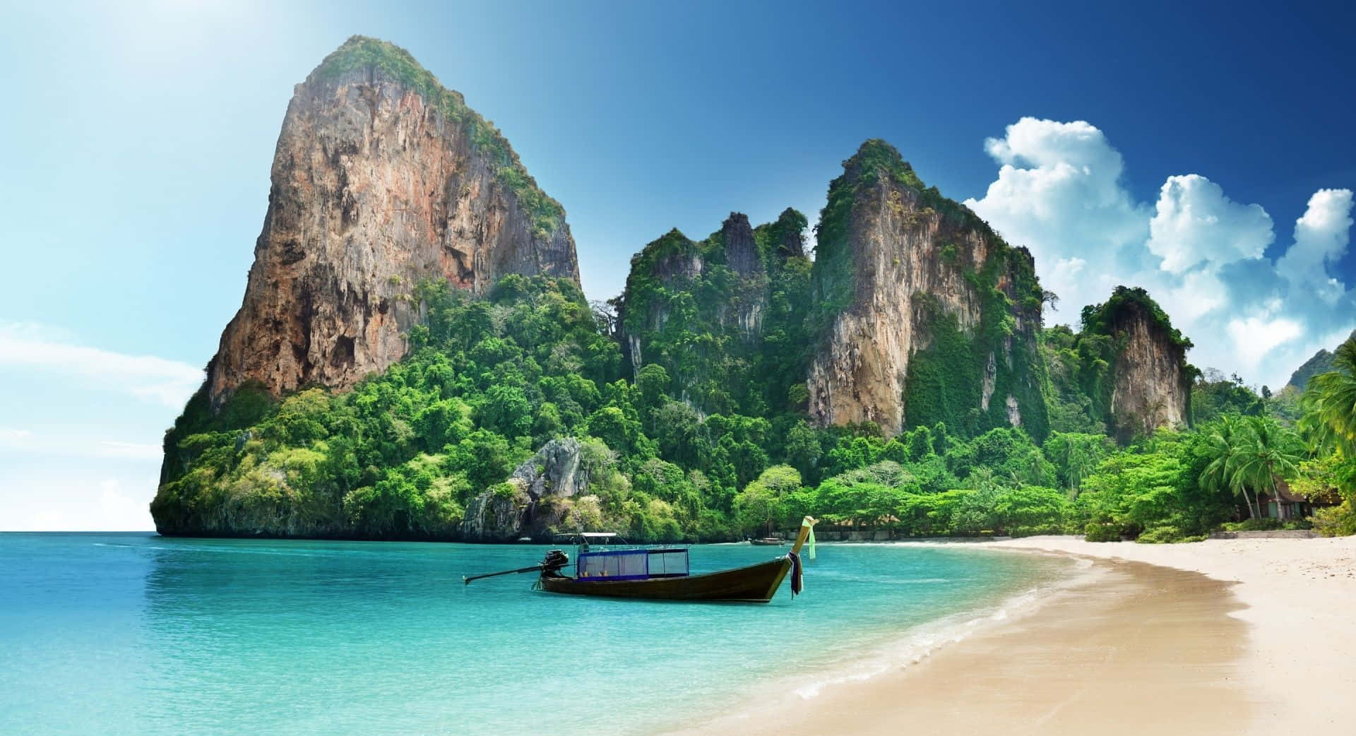 安達曼海海灘主題背景 壁紙 — 一艘長尾船停泊在碧綠色的海面上，旁邊是沙灘，沙灘被高聳的叢林覆蓋的石灰岩懸崖環繞，天空湛藍明亮。
