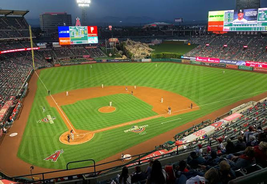 安那罕天使隊球場 MLB 分數板 壁紙 — 一場棒球比賽在球場燈光下展開，球員在場上，球迷在看台上，正值黃昏時分。