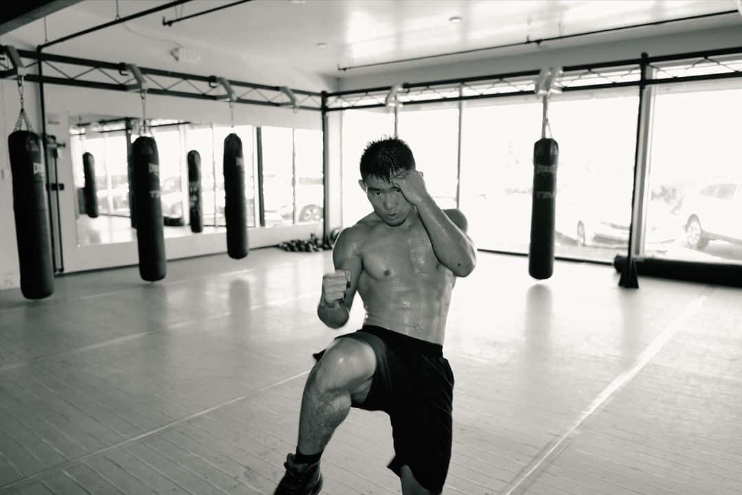 運動員在明亮的健身室中練習踢拳，使用重沙包。