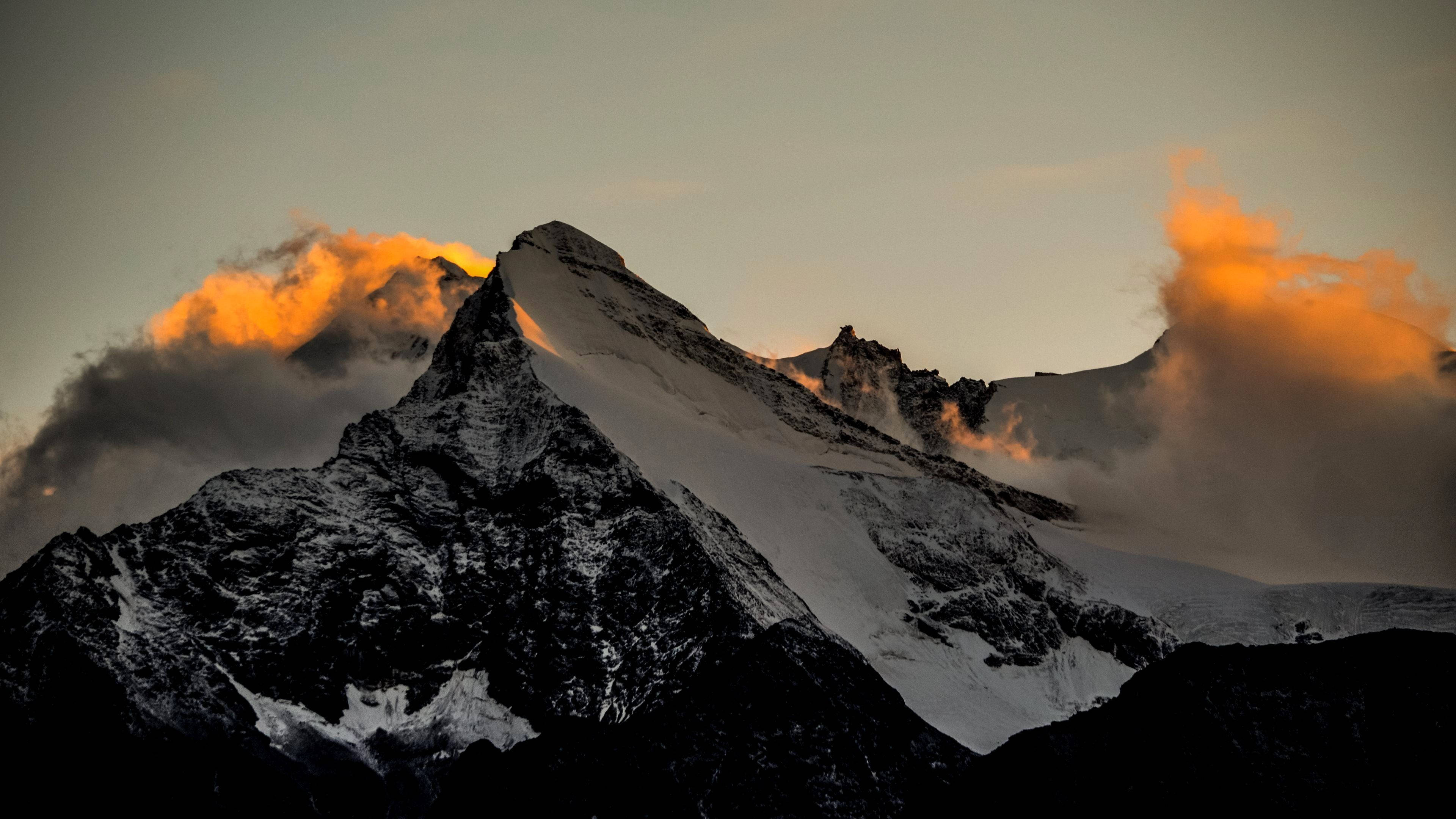 完美三角山峰 macOS 壁紙 — 白雪覆蓋的山峰刺穿暮色天空，金色光芒點燃其鋸齒狀山脊周圍的雲彩。