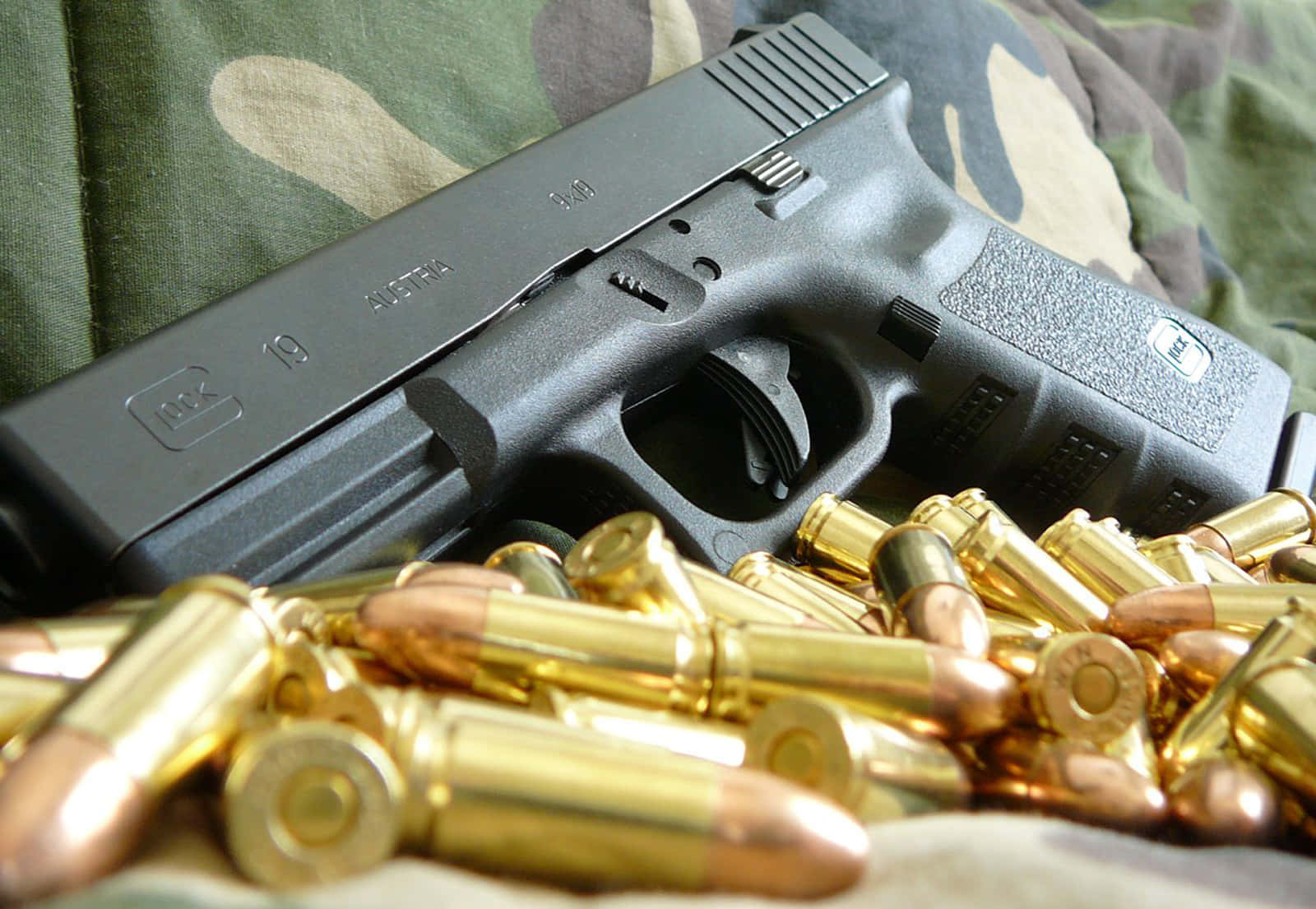 完美手槍 — 可靠的 Glock 19 壁紙 — 一把黑色Glock 19手槍放在迷彩布料上，周圍散落著黃銅彈藥。