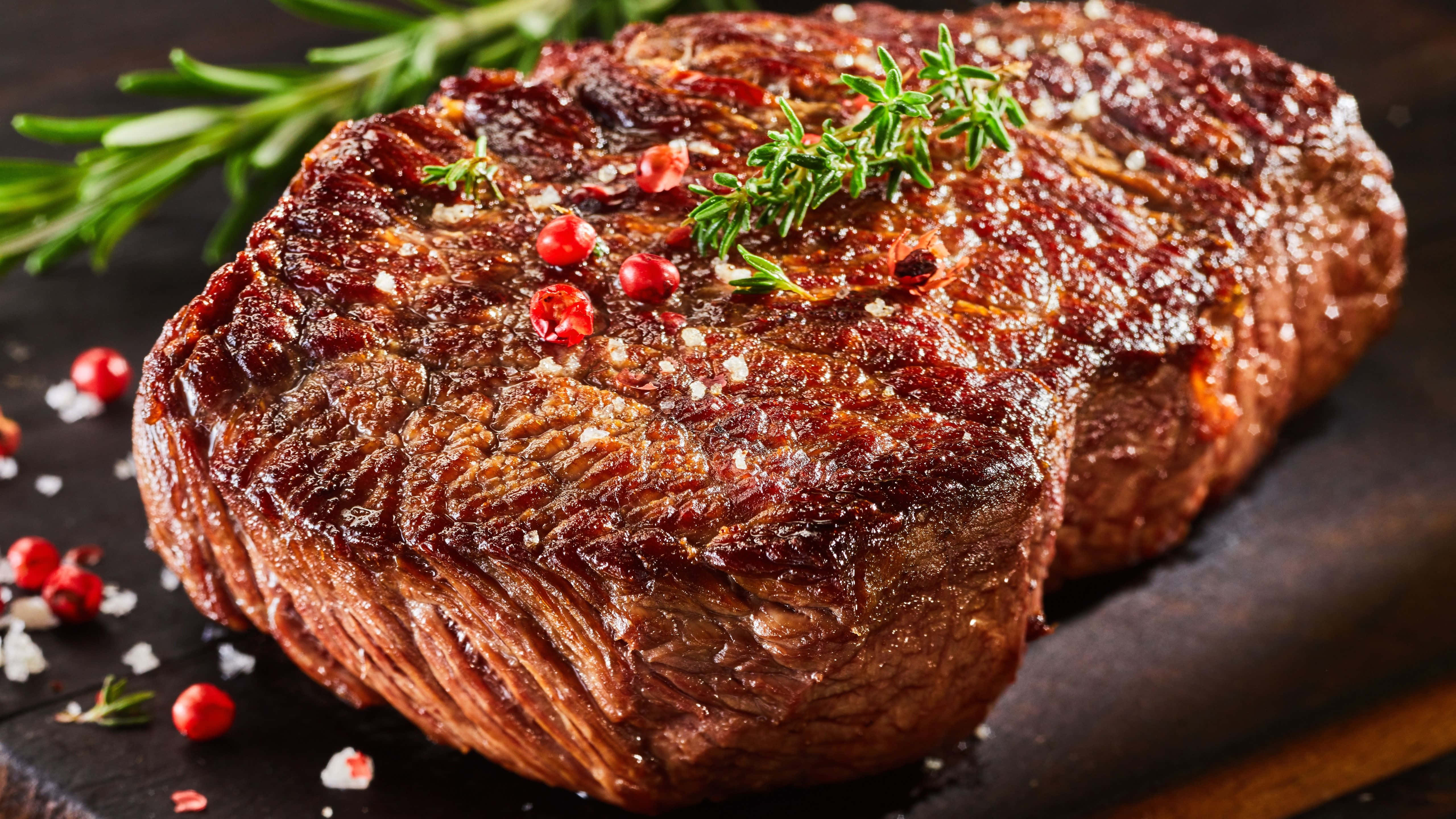 meat 桌布 壁紙 — 完美煎烤的牛扒閃爍著鹽和胡椒的光澤，配上新鮮迷迭香和紅胡椒粒，放在深色木板上。