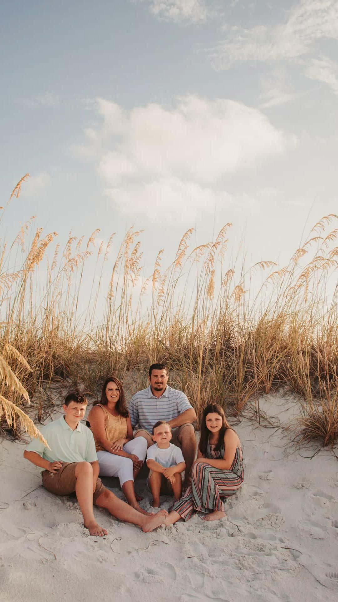 一個五口之家坐在沙灘上，身後有高高的草叢。