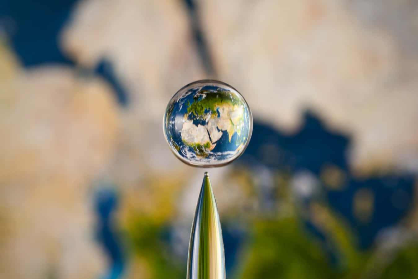 針尖上的水滴在模糊的地圖上反射出地球。