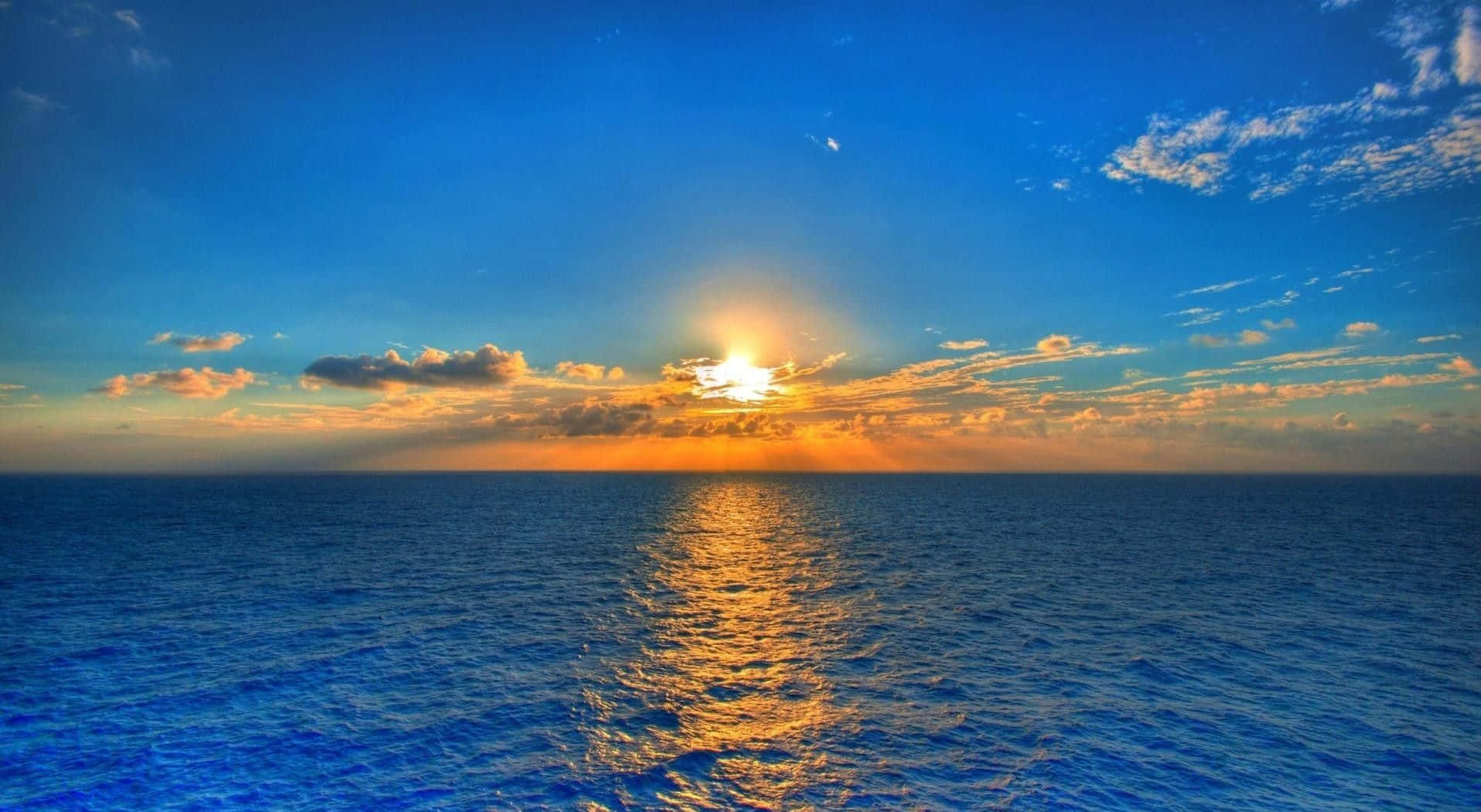 完美的海灘假期 壁紙 — 夕陽映照海洋，金色光線穿過雲層，反射在深藍色的水面上。