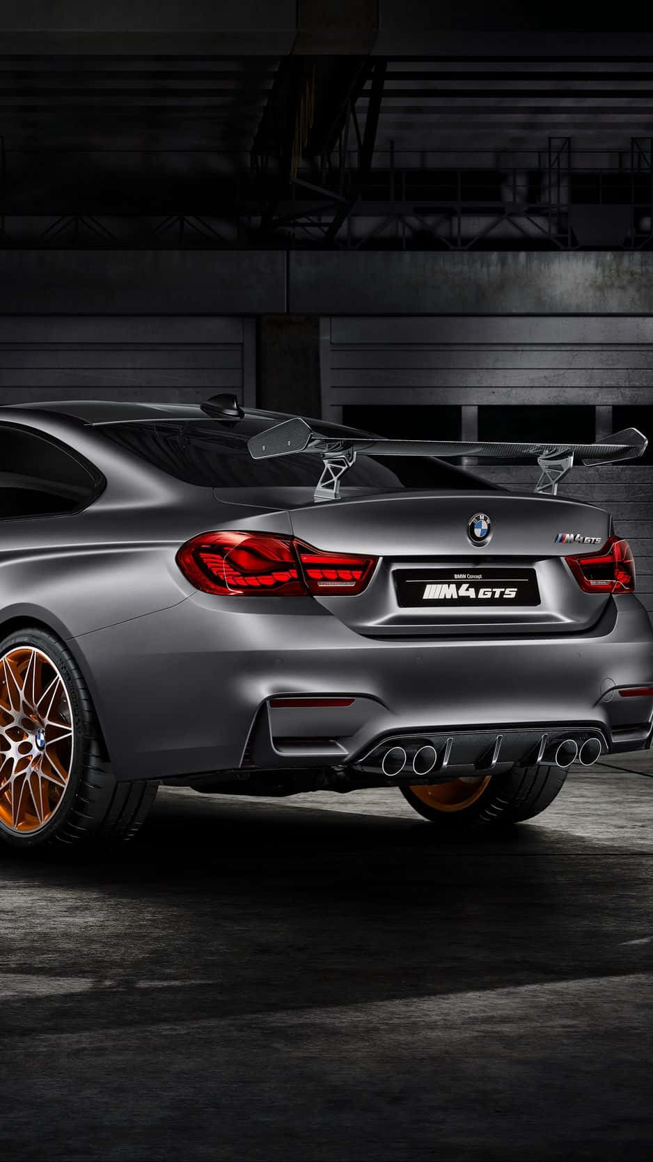 昏暗工業車庫中的啞光灰色BMW M4 GTS，配備銅色輪圈。