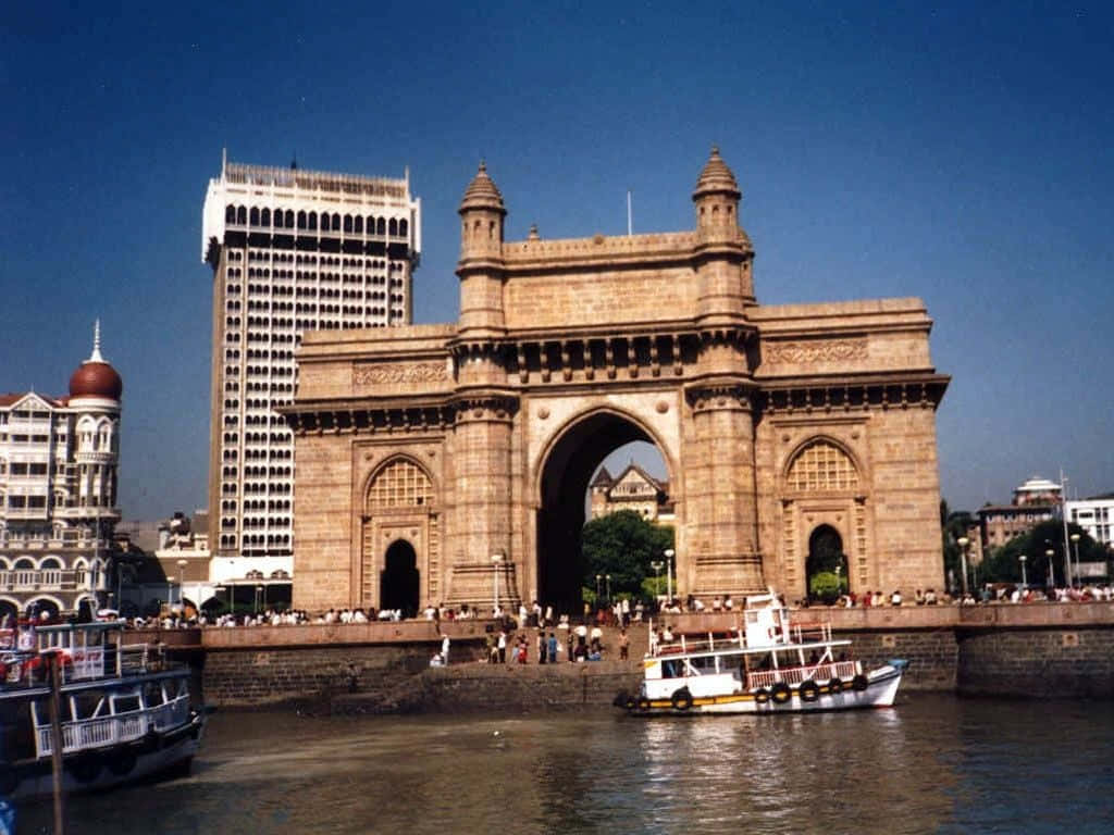 Mumbai 桌布 壁紙 — 宏偉的印度門紀念碑矗立在海濱，船隻在其拱門下穿行，天空湛藍。