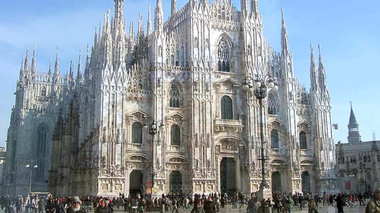Gothic Architecture 桌布 壁紙 — 宏偉的哥德式大教堂，擁有精緻的尖塔和雕像，在晴朗的藍天下高聳入雲，前景廣場上聚集了人群。