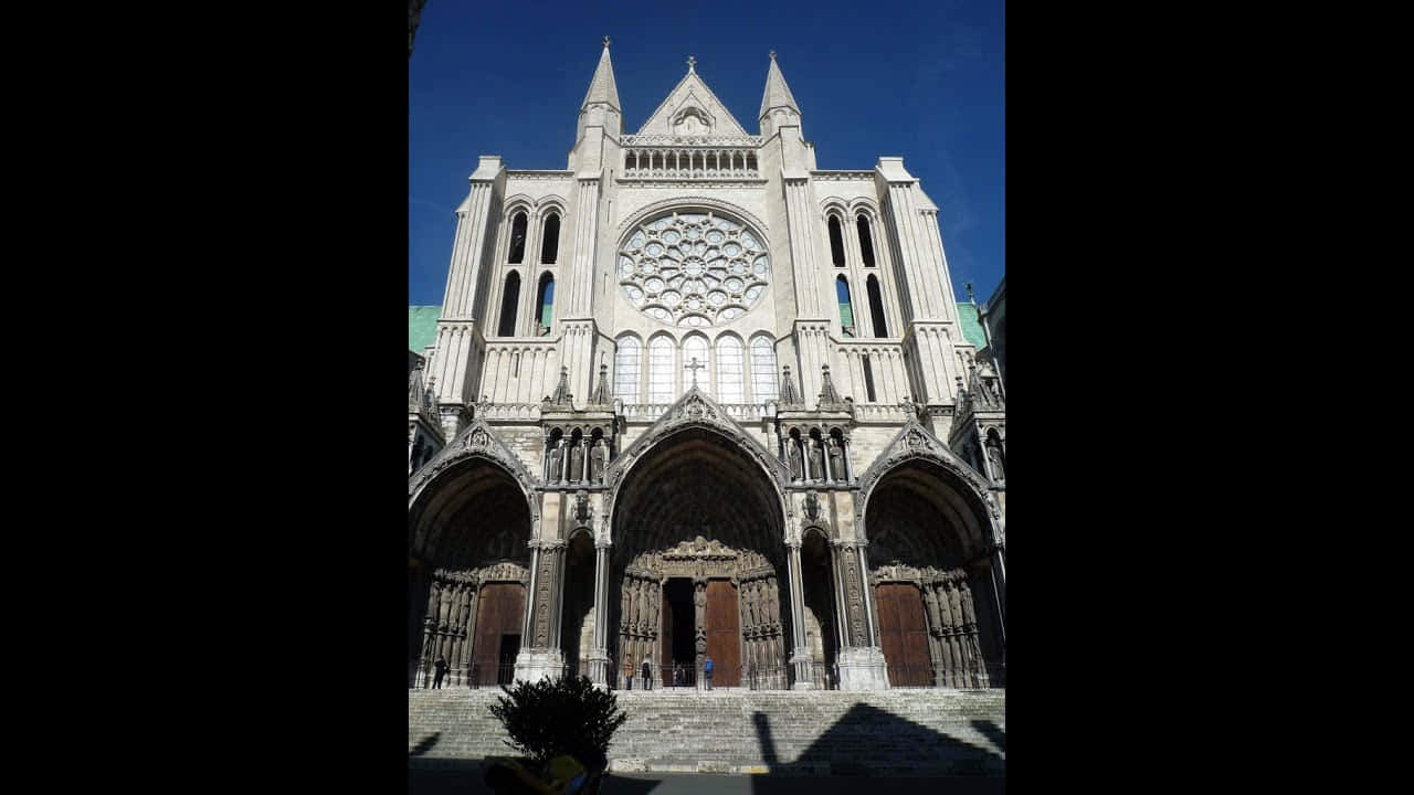 Gothic Architecture 桌布 壁紙 — 宏偉的哥德式大教堂正面，帶有玫瑰窗和尖頂，背景是清澈的藍天。