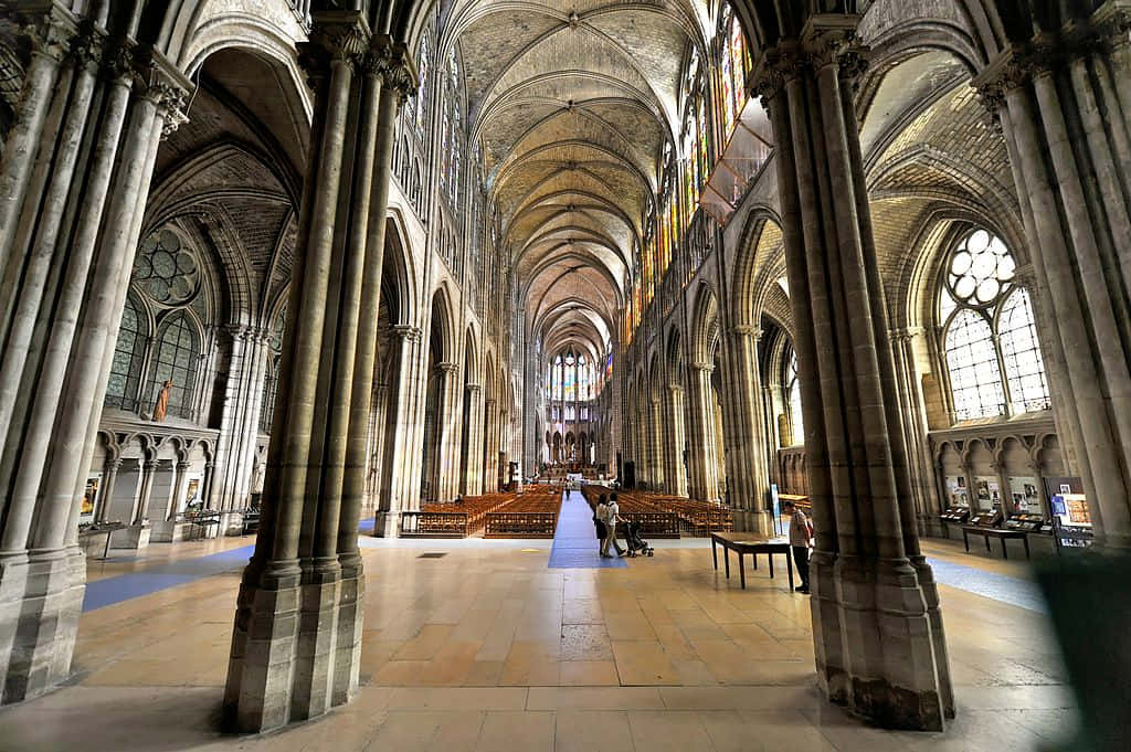 Gothic Architecture 桌布 壁紙 — 宏偉的大教堂內部，有高聳的石拱頂、彩繪玻璃窗，以及沿著中央走道行走的遊客。