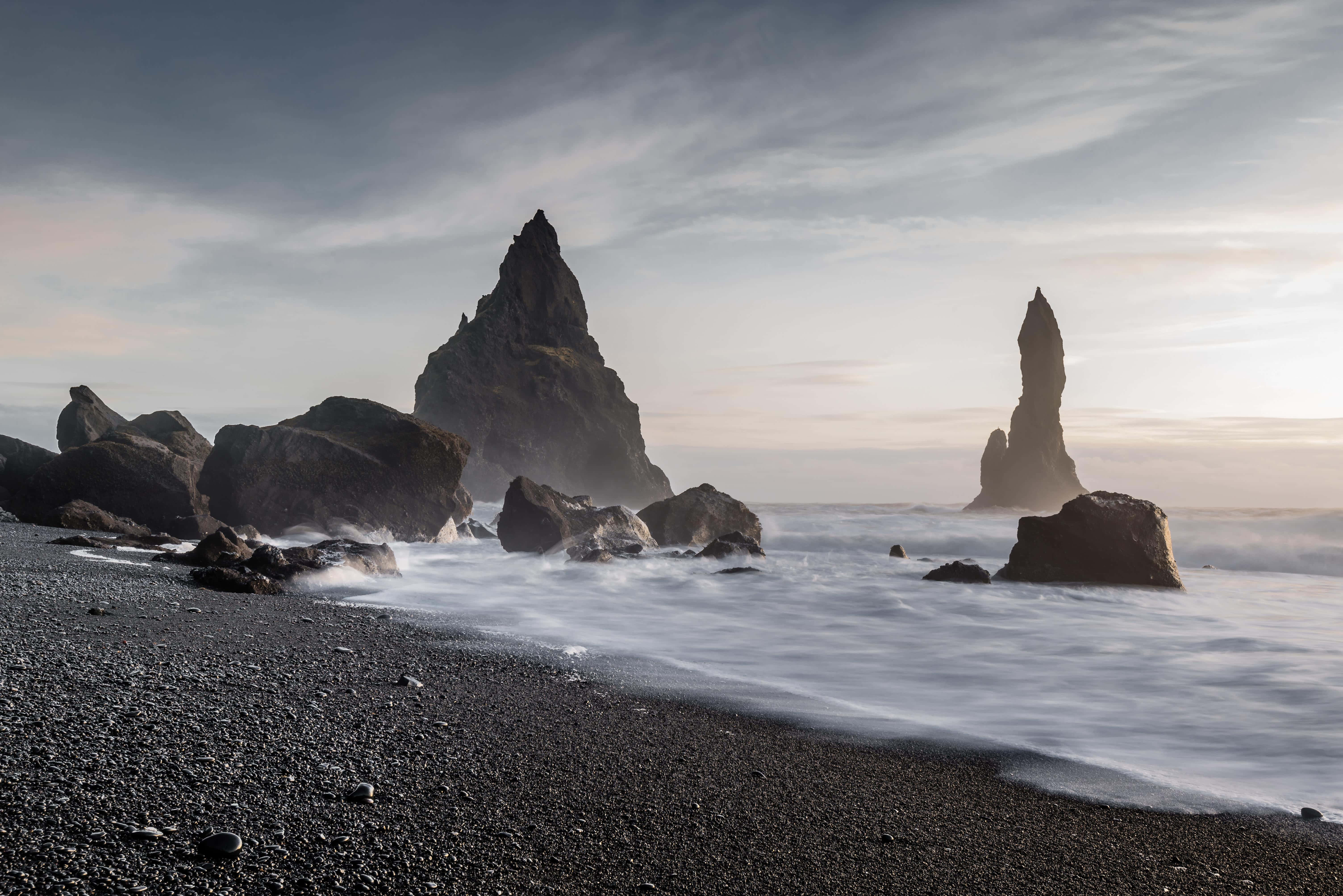 Black Sand Beach 桌布 壁紙 — 宏偉的海蝕柱從黑色火山沙灘上聳立，柔和的海浪在陰沉的暮色天空下拍打。