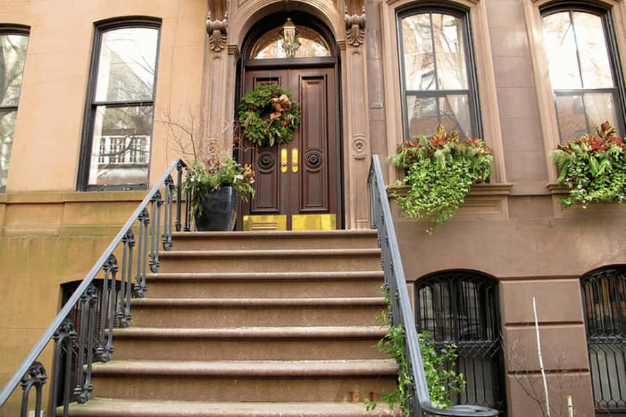 Brownstone 桌布 壁紙 — 宏偉的褐石入口，帶有華麗的鐵製欄杆、節日花環和茂盛的窗台花箱，襯托著莊嚴的木門。