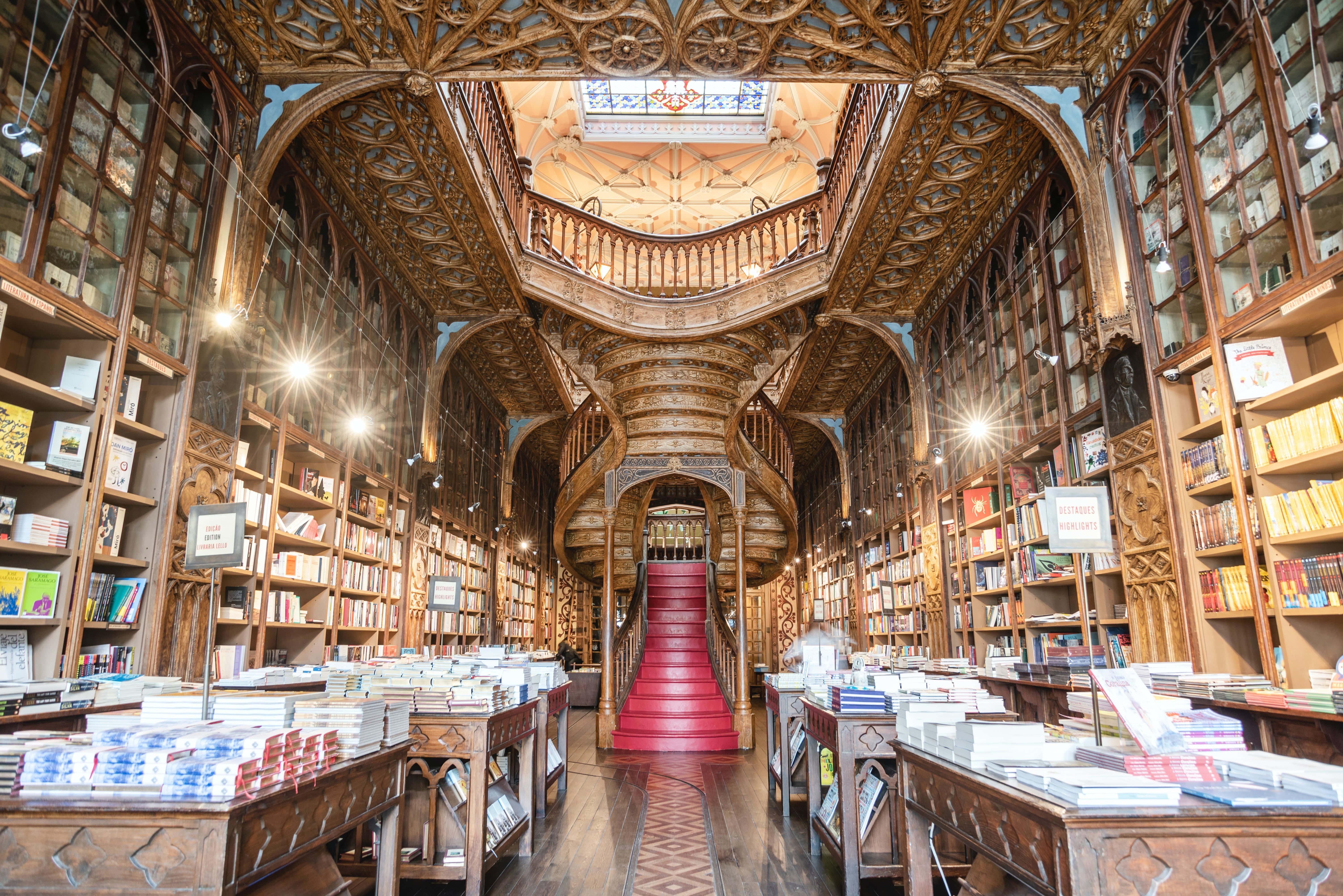 The Hogwarts Library 桌布 壁紙 — 宏偉華麗的圖書館，擁有高聳的木製書架、鋪有紅色地毯的寬闊樓梯，以及精緻的天花板細節。