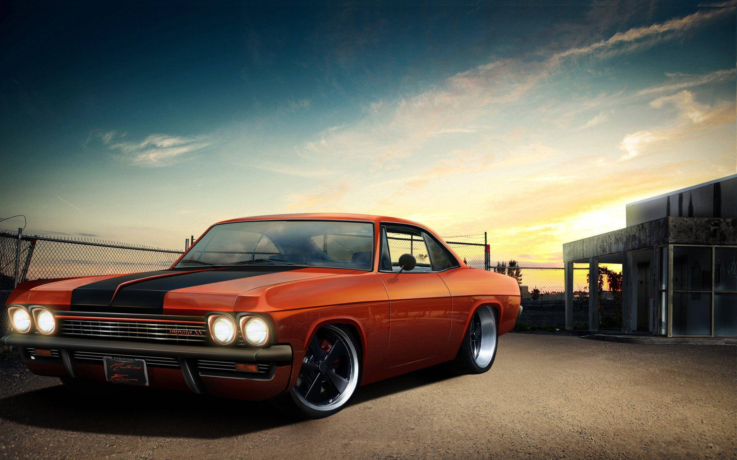 客製化 1967 年雪佛蘭 Impala 壁紙 — 一輛充滿活力的橙色經典肌肉車帶有黑色條紋，在夕陽天空下閃閃發光，旁邊是鐵絲網圍欄和混凝土建築。