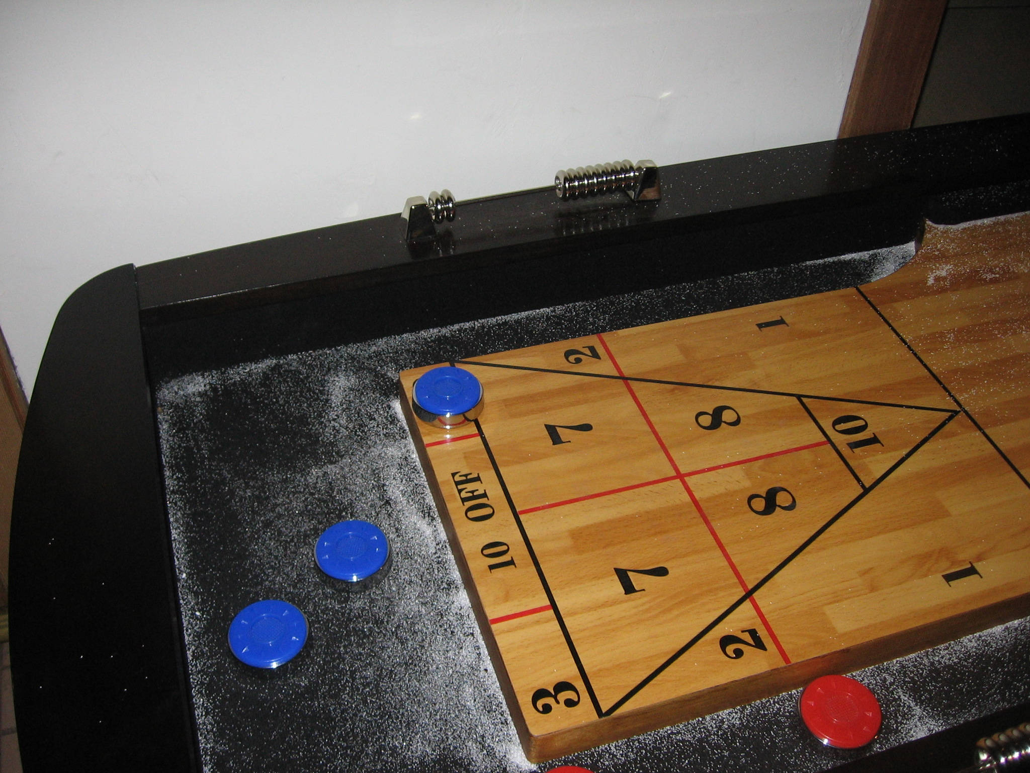 室內 Shuffleboard 桌與粉末 壁紙 — 一張沙狐球桌的特寫，木製計分區上撒有粉末，並有藍色和紅色的冰球。