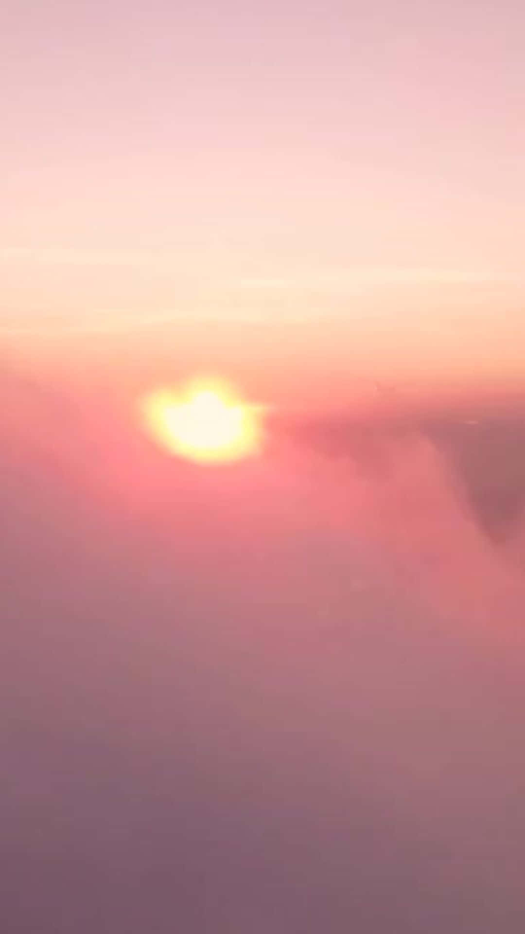 從空中俯瞰，朦朧雲層上帶有柔和粉紅色和橙色色調的日落