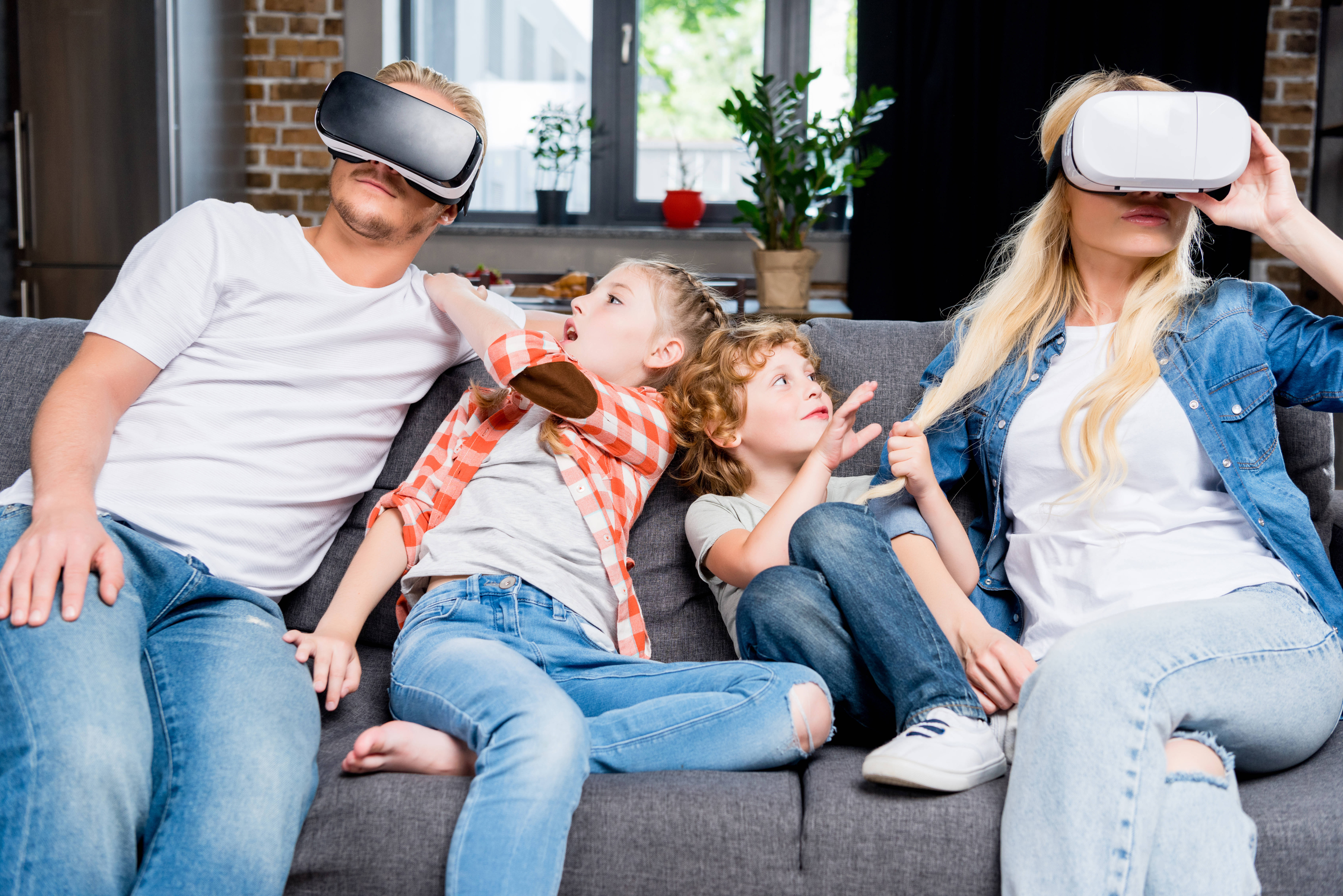 家庭玩 VR 壁紙 — 一家四口坐在梳化上戴著VR頭盔，兩個孩子興奮地指向虛擬體驗並做手勢。