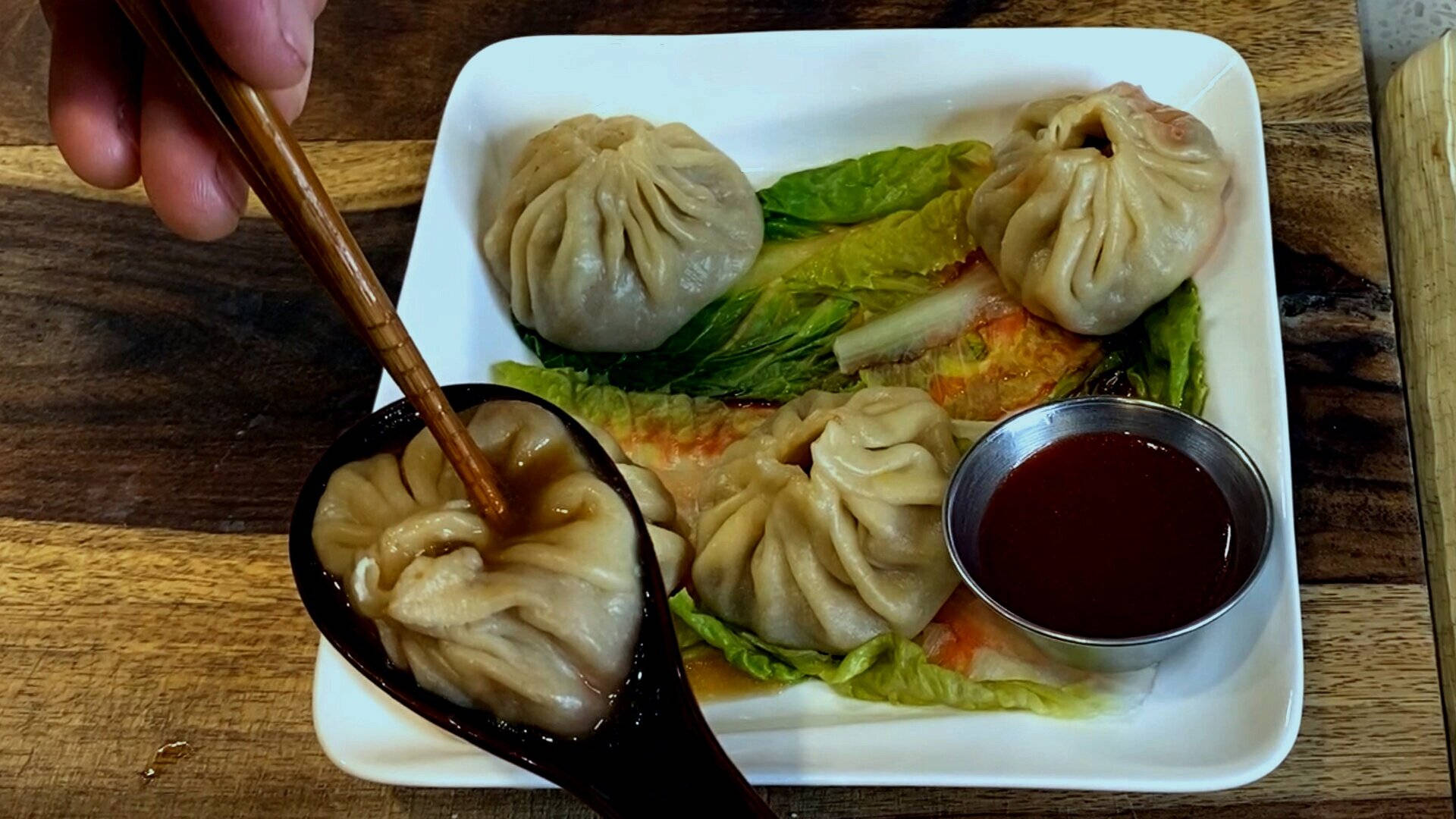 手用筷子從有生菜和醬的碟中夾起餃子。