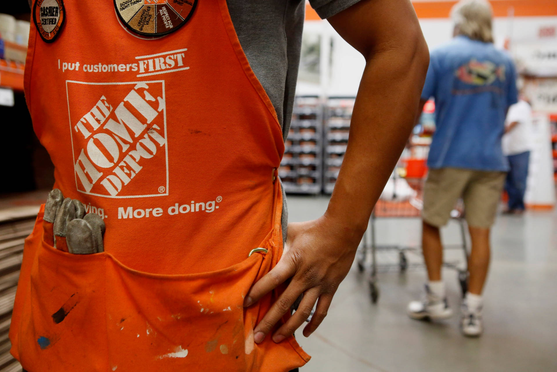 身穿橙色圍裙的 Home Depot 工人在商店通道中拿著工具。