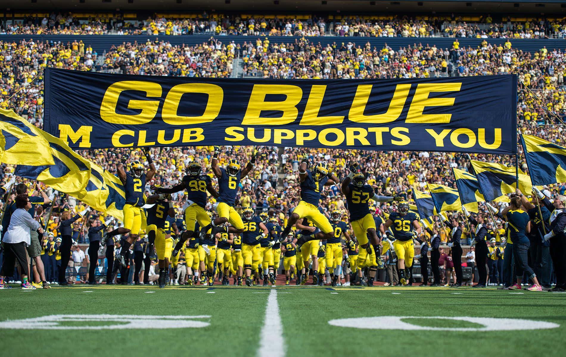 足球隊在球場上慶祝，球迷揮舞旗幟並舉著「Go Blue」橫幅。