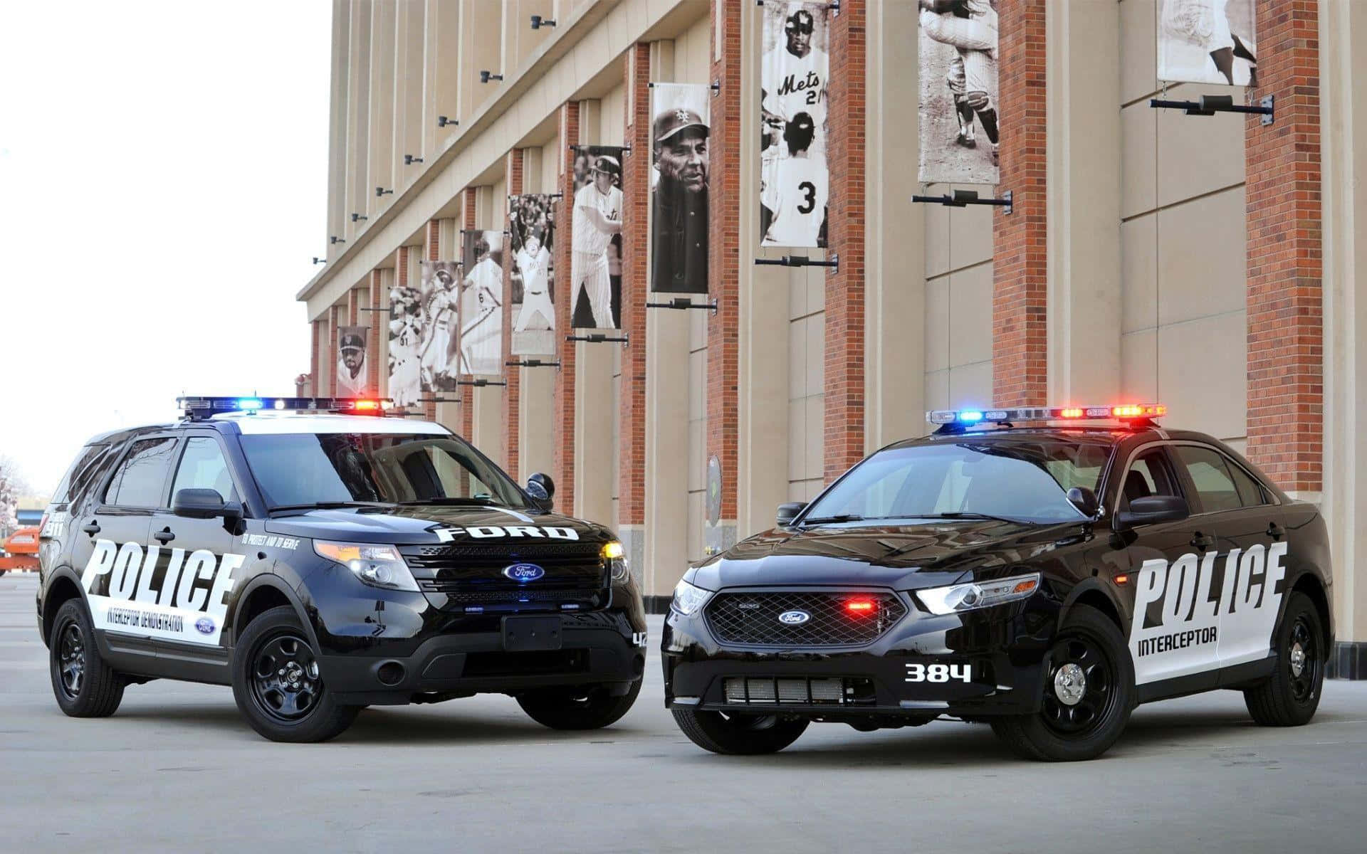 兩輛警車停泊在一個有選手橫額的棒球場外。