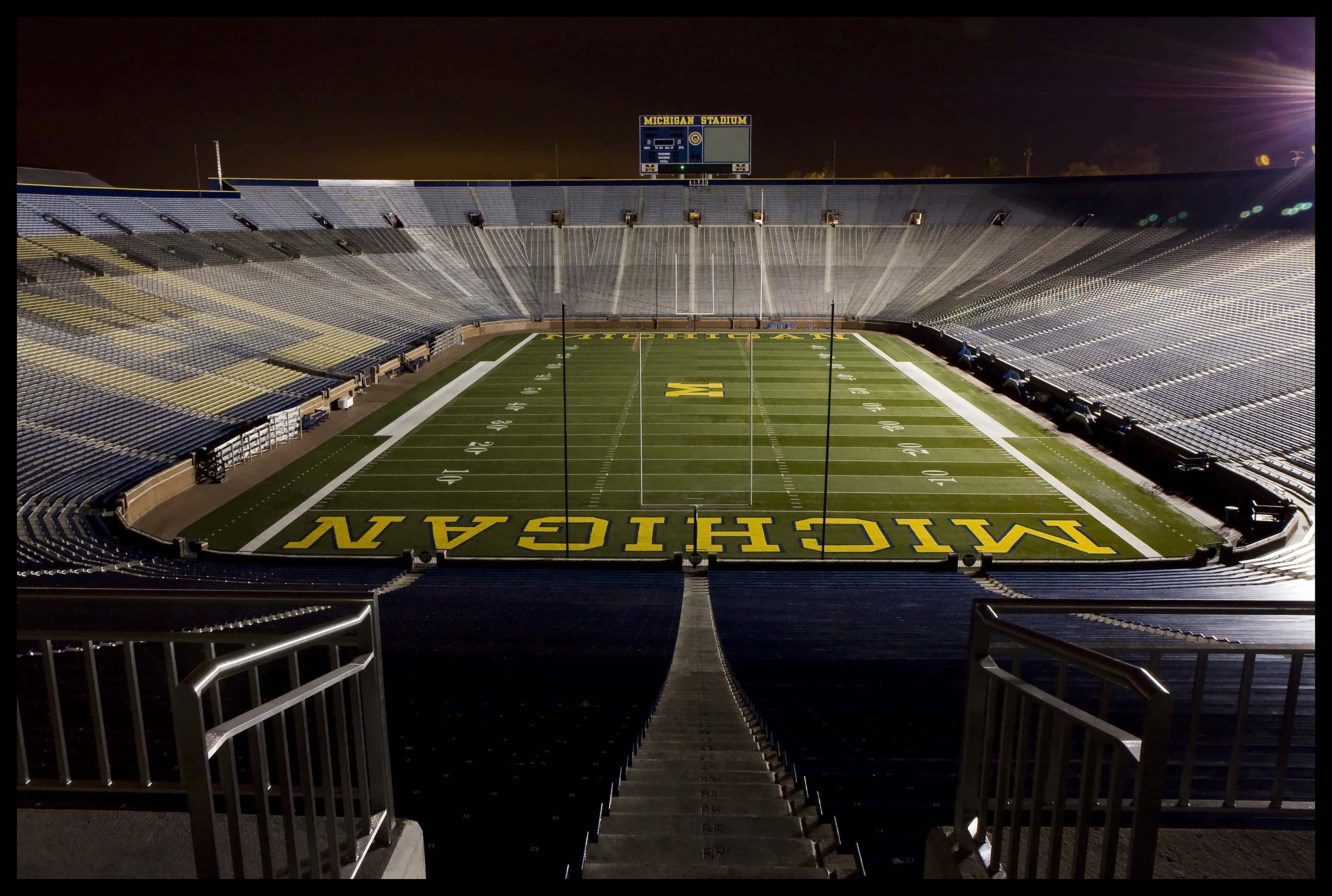 Michigan Wolverines 桌布 壁紙 — 密歇根體育場空無一人的足球場在明亮體育館燈光照射下的戲劇性夜景。