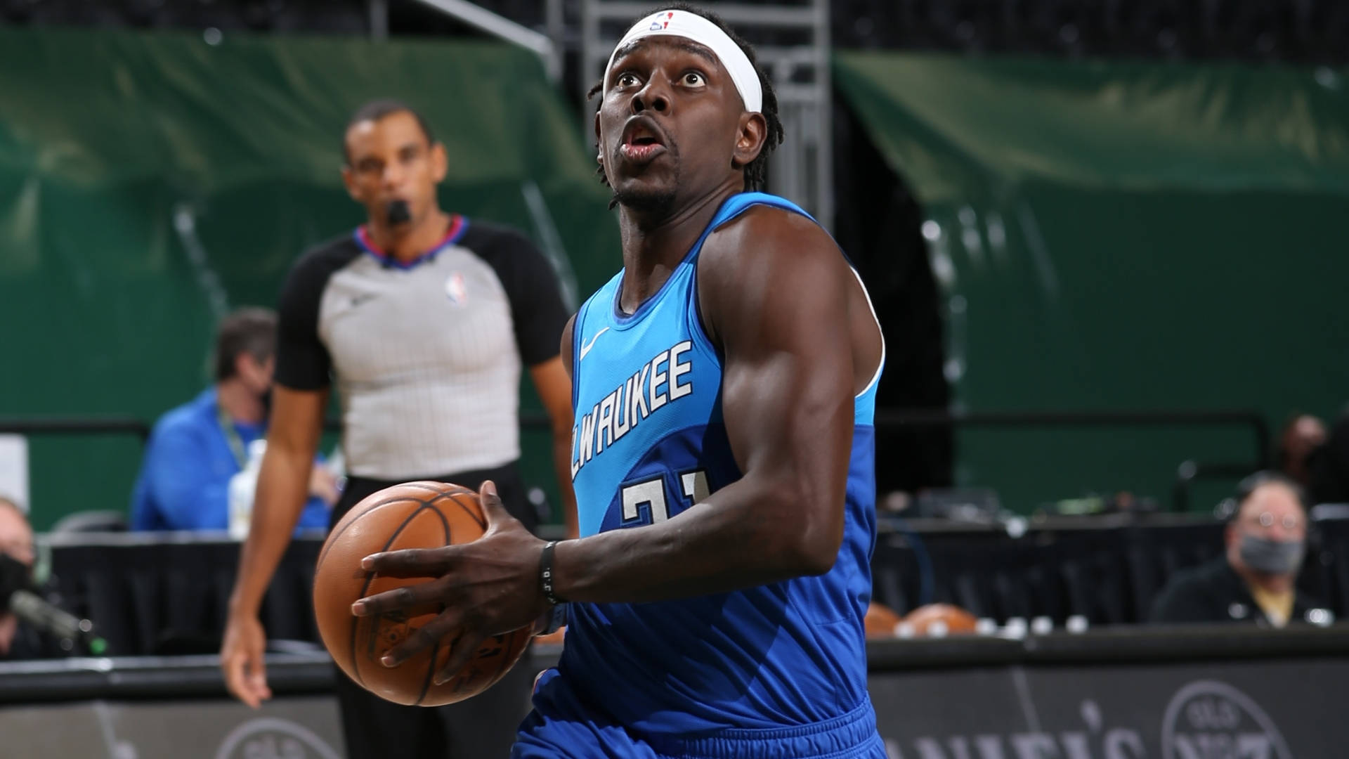 密爾瓦基控球後衛Jrue Holiday 壁紙 — 一位身穿藍色球衣的密爾沃基公鹿籃球運動員在比賽中專注地運球。